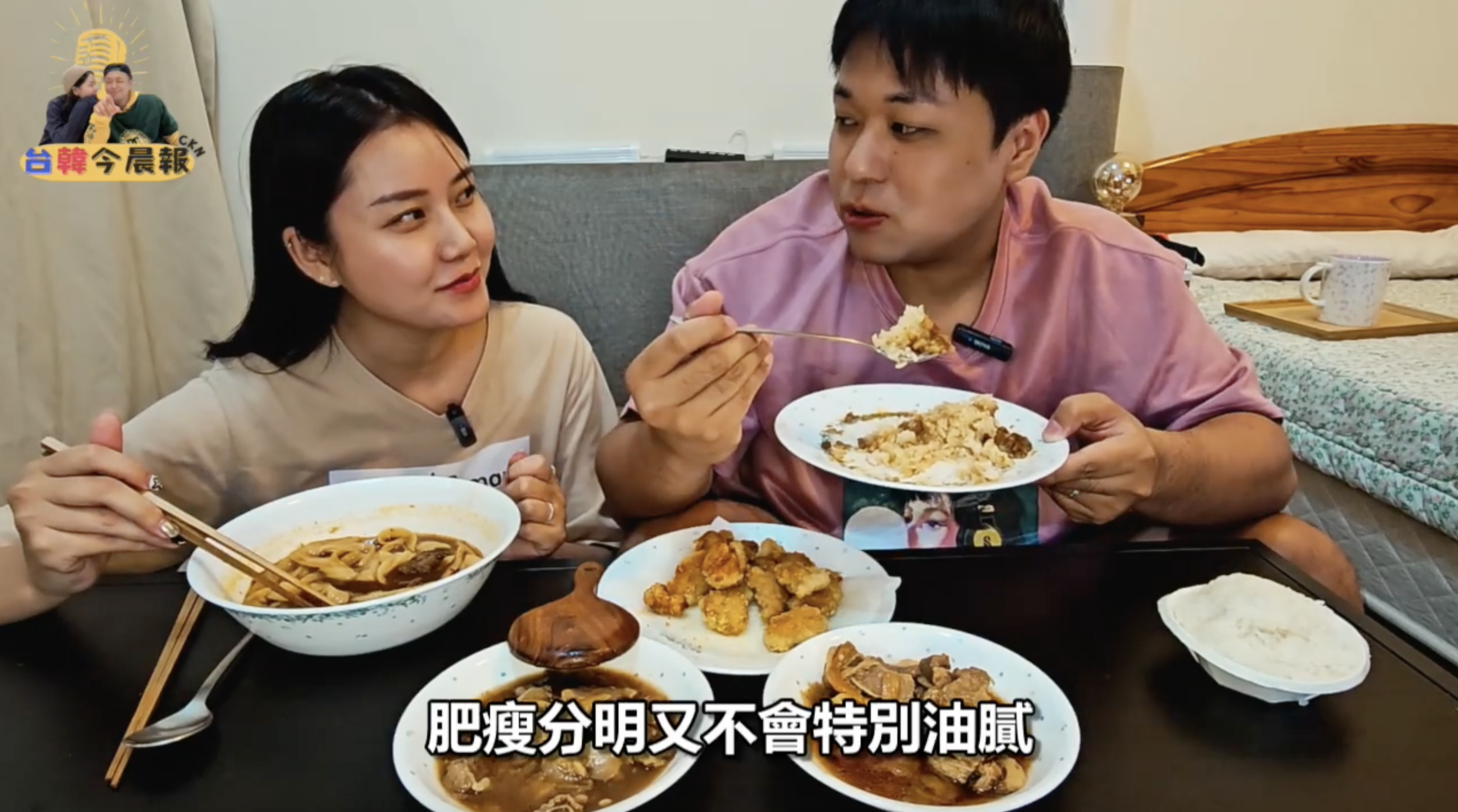 年輕男女繼續品嚐食物。男性正在用筷子夾起一些食物，女性則看著他。桌上的菜餚依然豐富。畫面下方有字幕"肥瘦分明又不會特別油膩"。