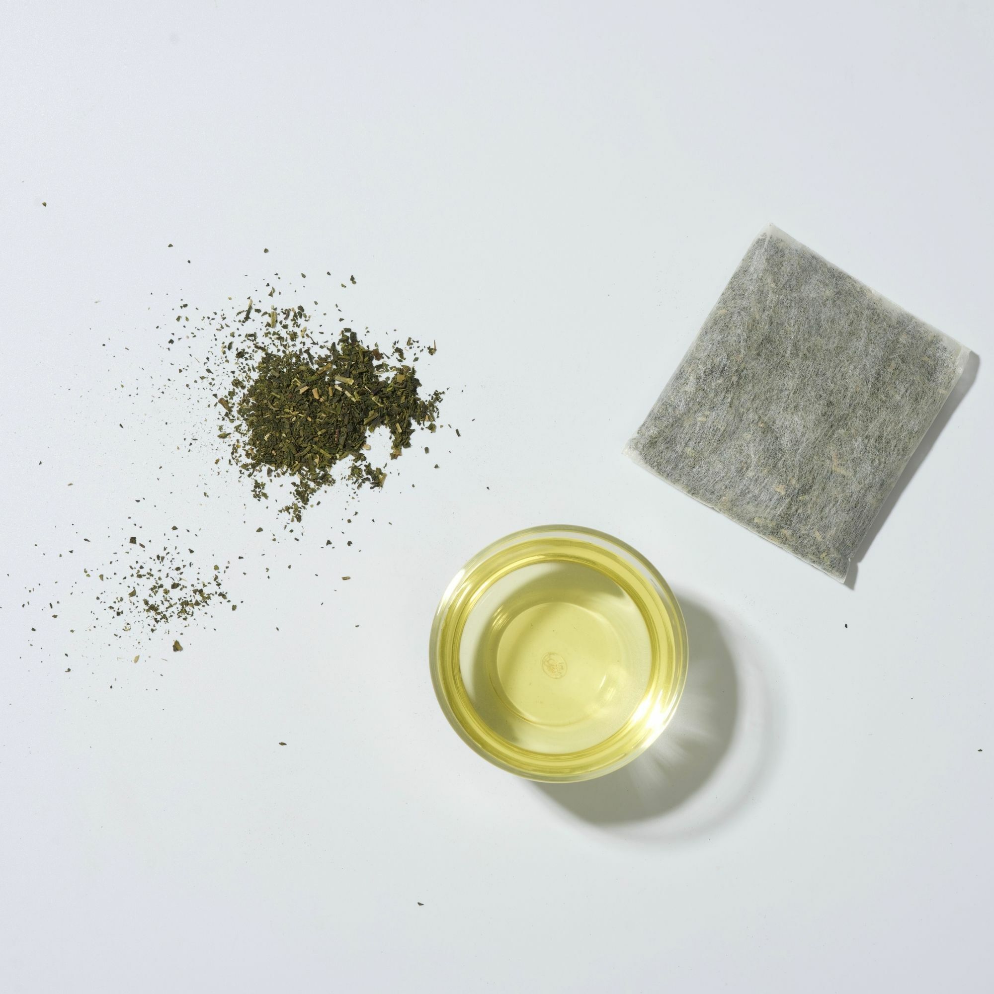 照片上呈現,炒菁綠茶茶葉、大茶包與綠黃色茶湯