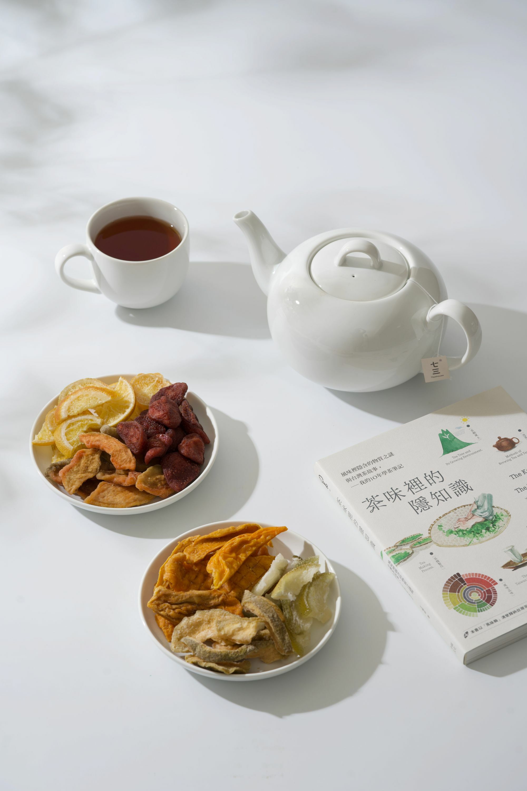 畫面裡，有茶壺、茶杯、台灣果乾、與書本「茶味裡的隱知識」呈現完美的午茶時光氛圍。