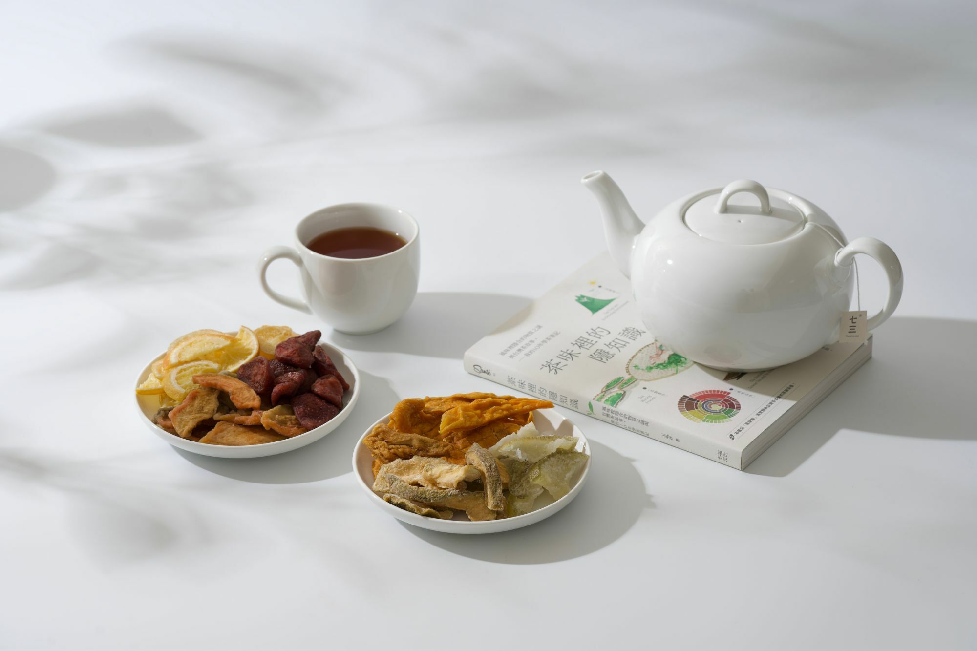 畫面裡,有茶壺、茶杯、台灣果乾、與書本「茶味裡的隱知識」呈現完美的午茶時光氛圍。