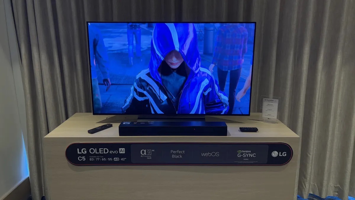 LG C5 OLED 智能電視展示中，屏幕顯示一個穿著帶兜帽藍色外套的角色，強調高對比度和精確細節還原。電視放置於展示台上，展示台標示了產品功能，例如OLED evo AI、Perfect Black、webOS 和 NVIDIA G-SYNC 支援等，專為遊戲和沉浸式體驗設計。