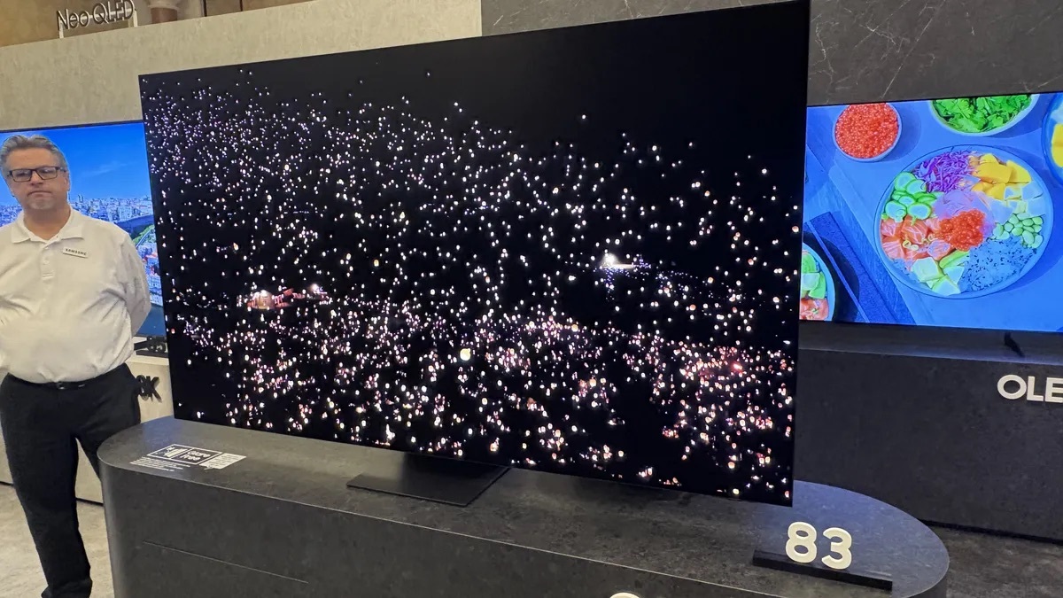 Samsung S95F OLED 智能電視顯示器展示現場，畫面呈現出極致的黑色背景和明亮的燈光點，突顯OLED技術的卓越對比度和深邃黑色表現。電視旁邊展示了其他Samsung產品，吸引觀眾對高端顯示技術的注意。