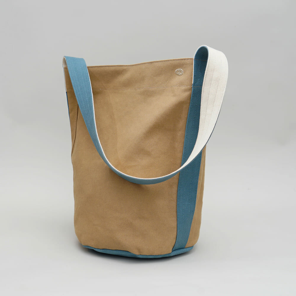 阿福圓筒帆布包正面展示，褐土色調與立體圓柱設計，適合日常與旅行使用