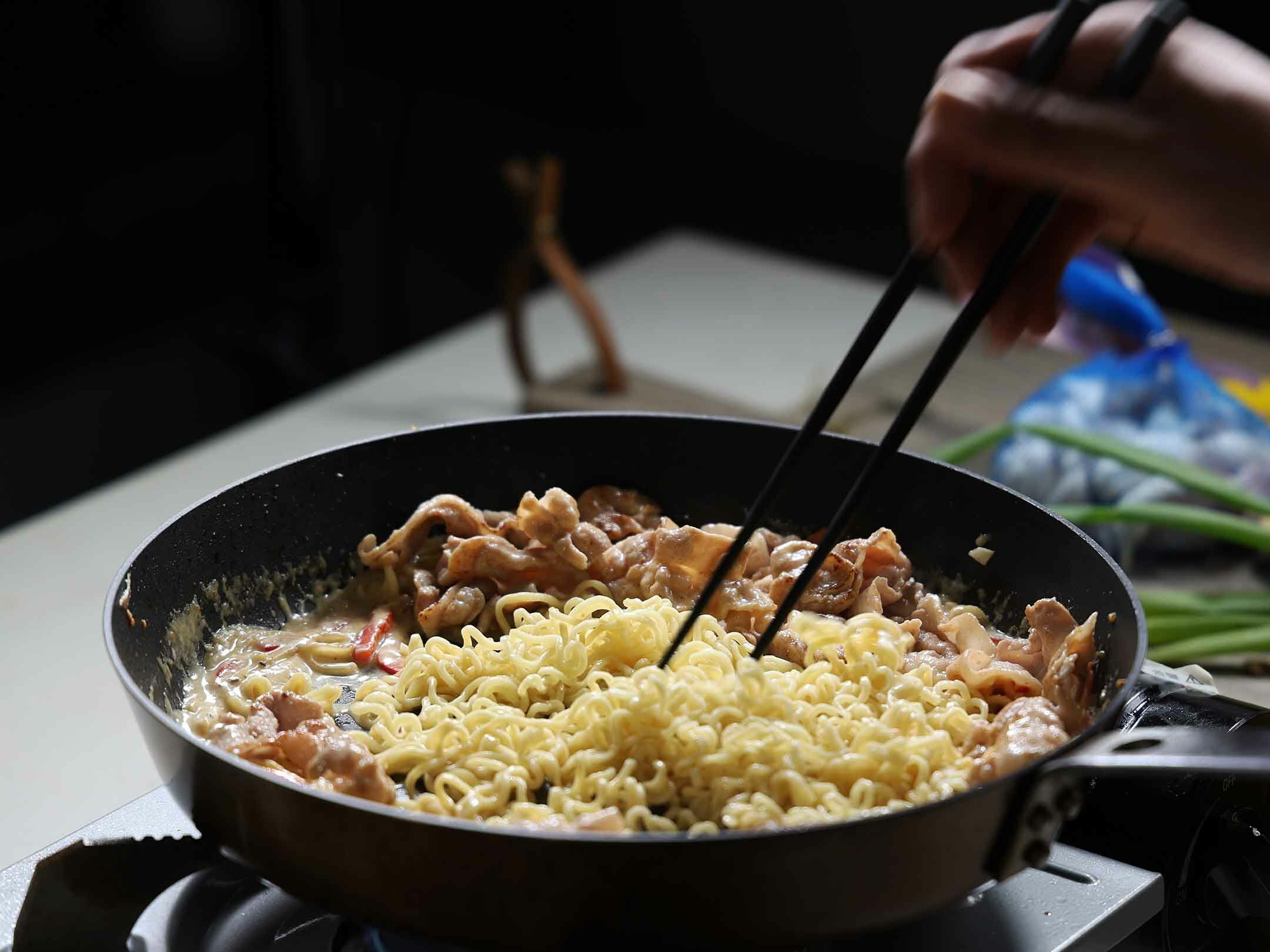 將煮好的泡麵和煎好的五花肉片放入鍋中，與咖哩醬汁充分拌炒均勻。