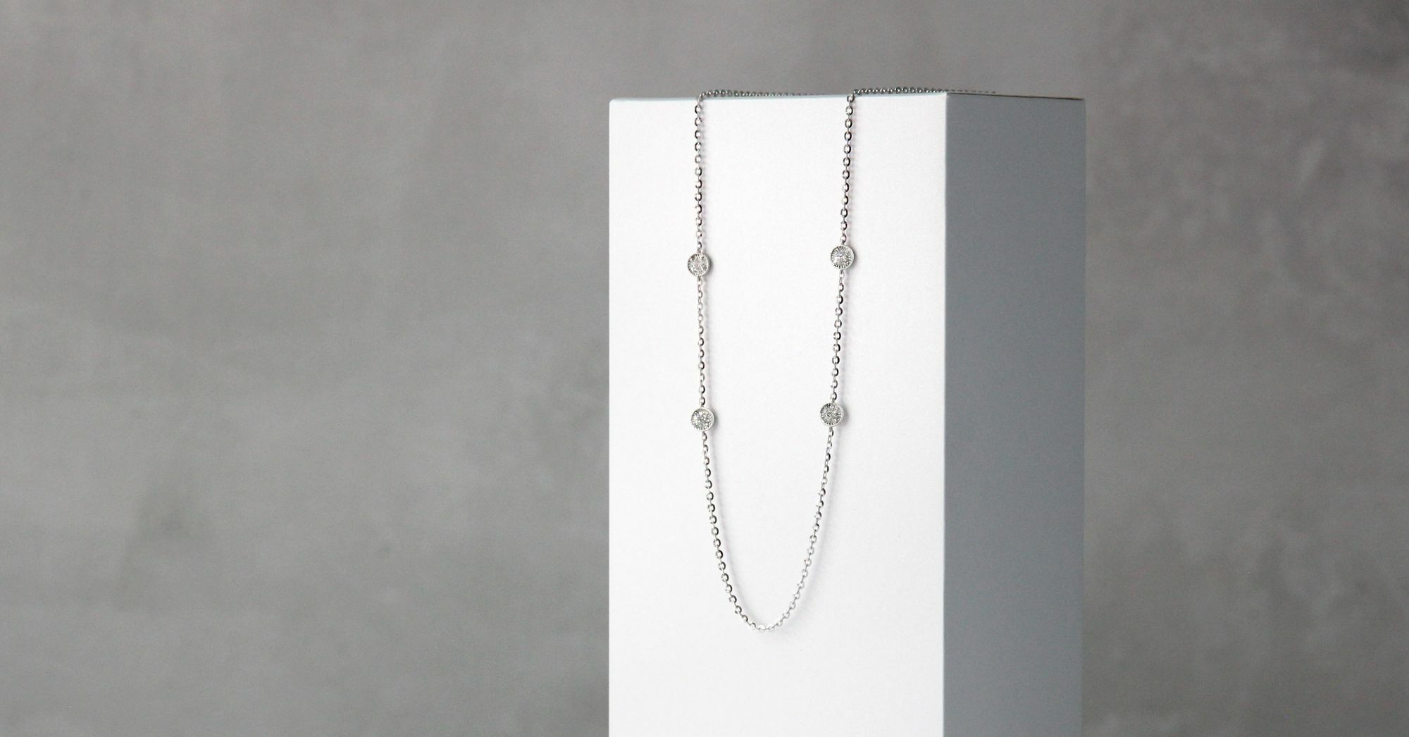 A delicate 18K gold necklace with small diamonds set at intervals, displayed against a gray background.