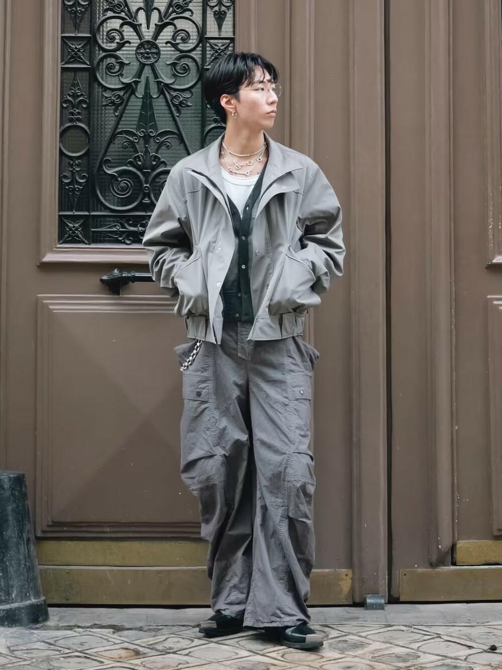 男生日系時尚穿搭,身著 SUBLATIONS 灰色外套搭配工裝風寬褲,腳踩 Achilles Ion Gabriel 黑色靴款,整體灰階造型層次豐富,展現都市型男的個性魅力。