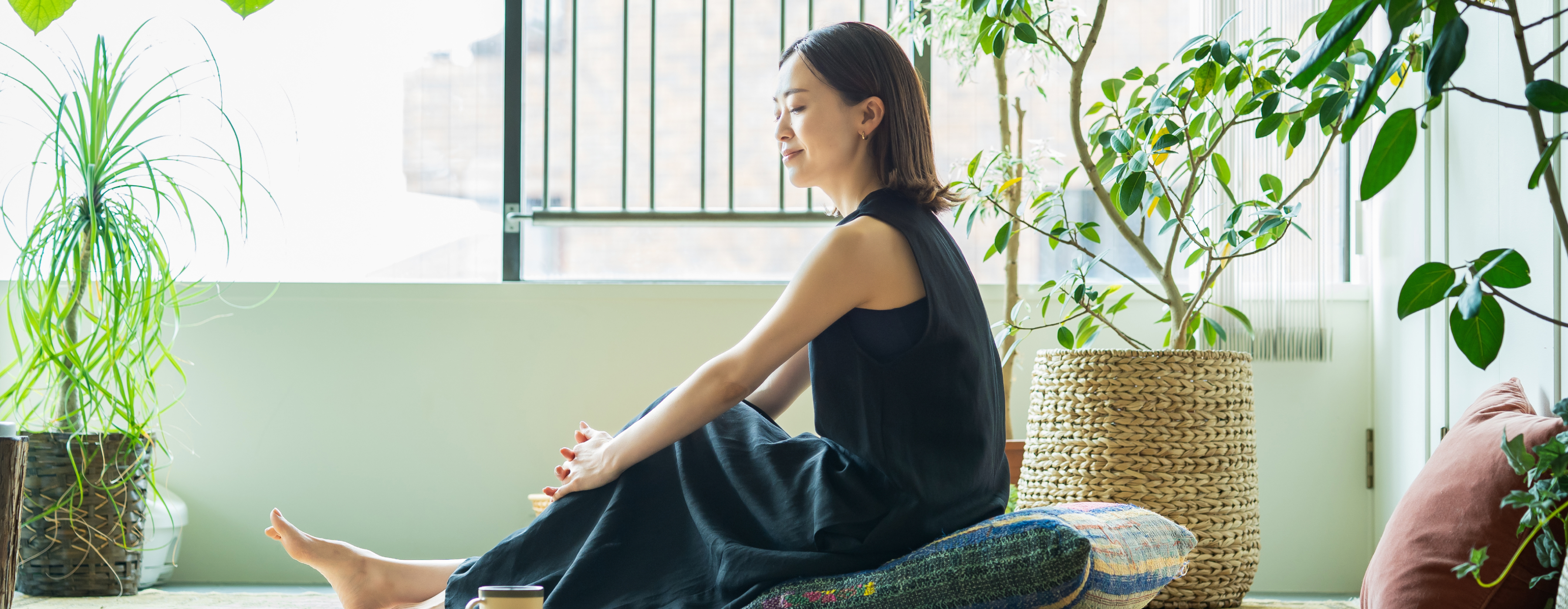 一位女性坐在綠意盎然的窗戶旁，享受日光，表情愉悅滿足。