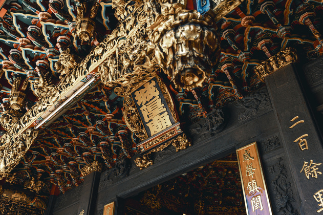 圖片展示的是新竹都城隍廟的精緻廟宇門廊。畫面中可以看到廟門上方華麗的木雕裝飾，細緻的雕刻和金色元素凸顯出廟宇的莊嚴與神聖。