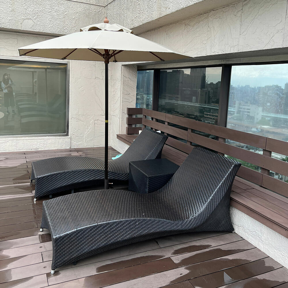 現代風格的露天陽台，擺放兩張黑色藤編躺椅與一支遮陽傘