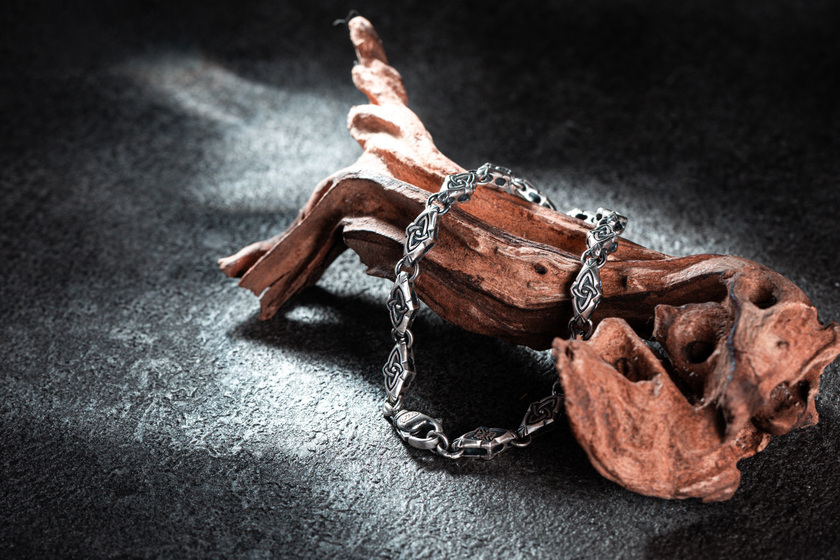 時光之鏈 純銀手鍊 The Chain of Time Silver Bracelet，手鍊以凱爾特三位一體結元素連結成鏈，象徵生命經驗與靈魂片刻的串聯，純銀質感與結構設計展現時間流動之美，圖為產品靜置於木質紋理與石面背景上拍攝
