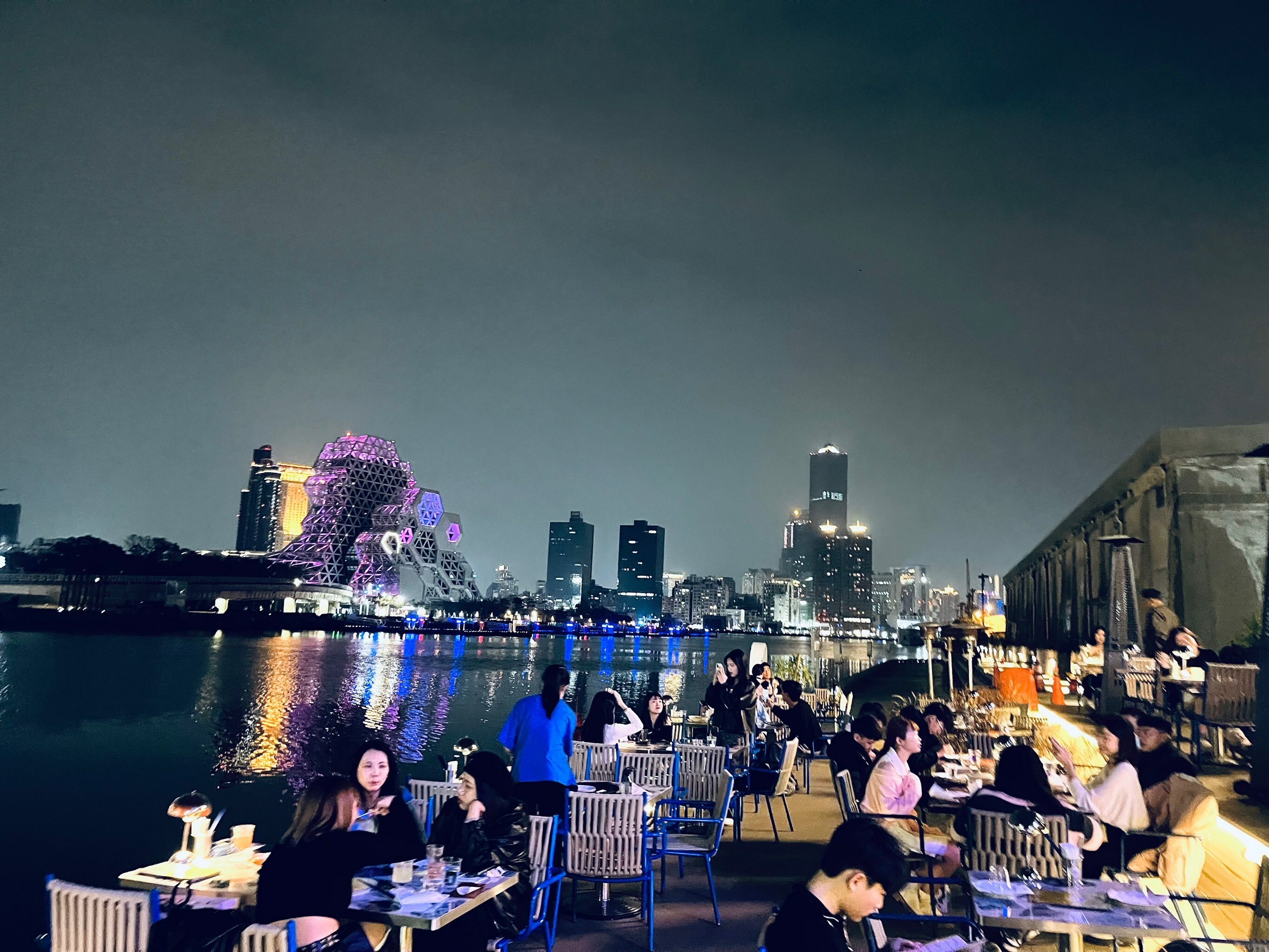 永心浮島 YONSHIN FUDOPIA 河畔露天座位區,遠景可見高雄流行音樂中心與城市燈火,夜晚用餐浪漫氛圍