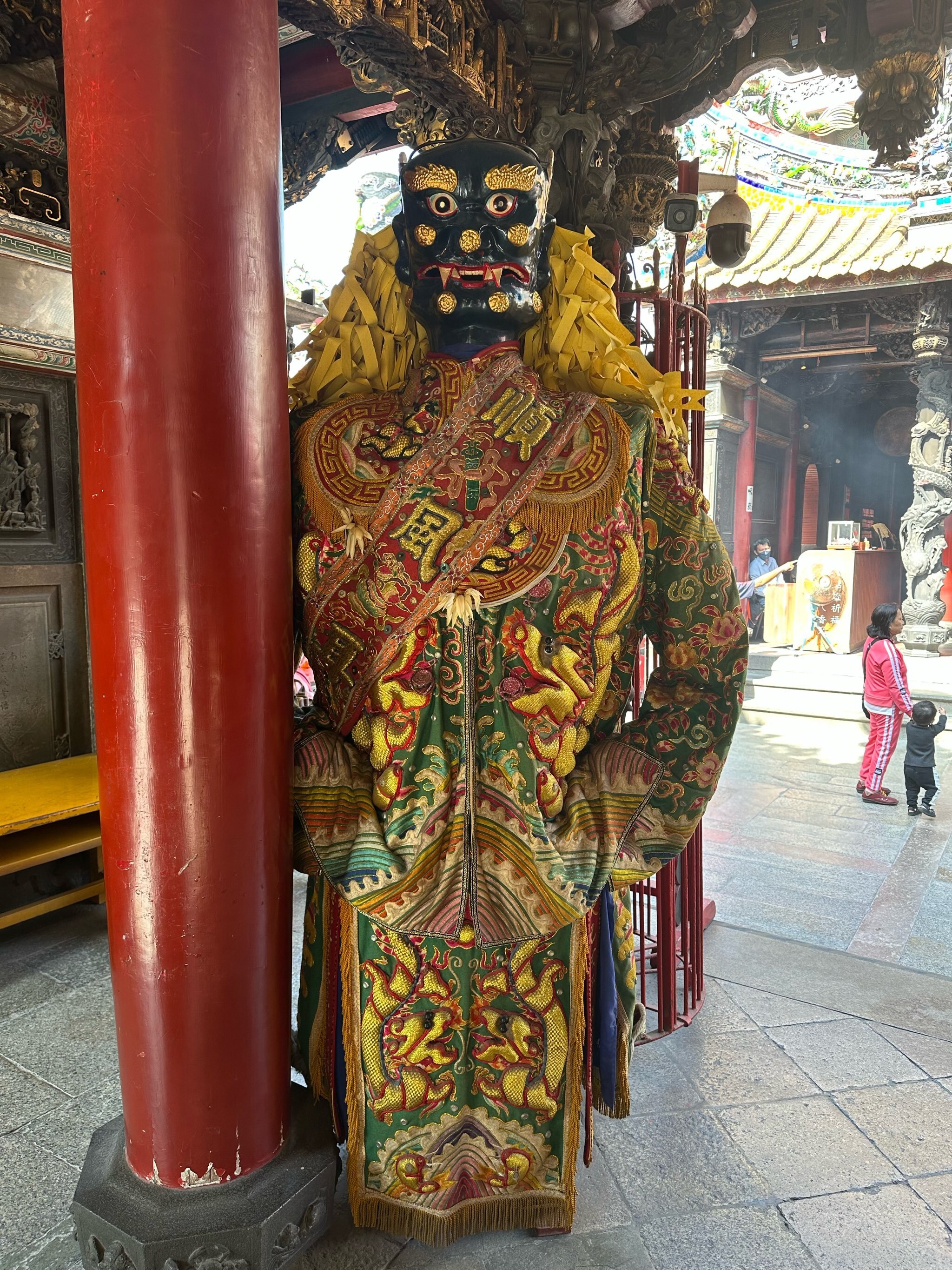 北港朝天宮黑臉門神立於紅柱旁,身著龍紋服飾,展現台灣傳統廟會文化特色