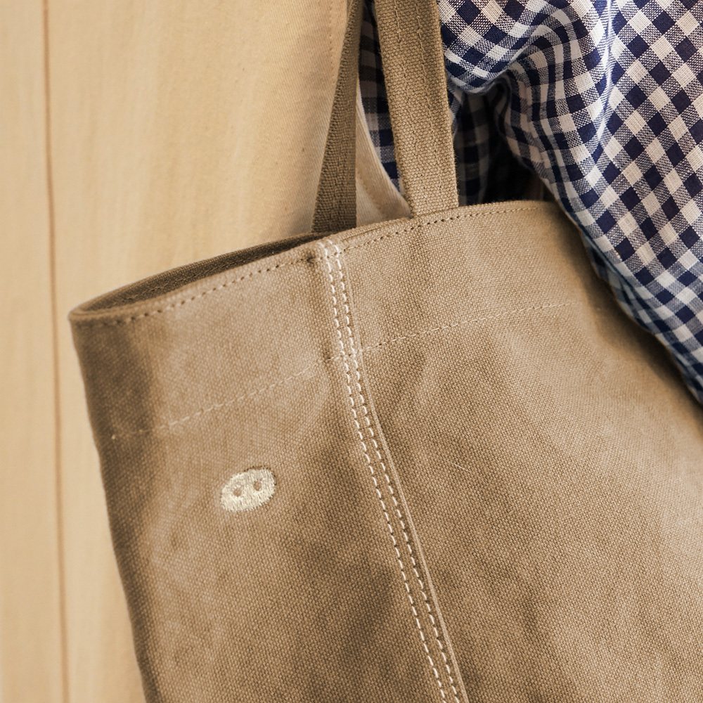 褐土帆布包細節特寫，展示金屬拉鍊、厚磅帆布與精緻縫線質感