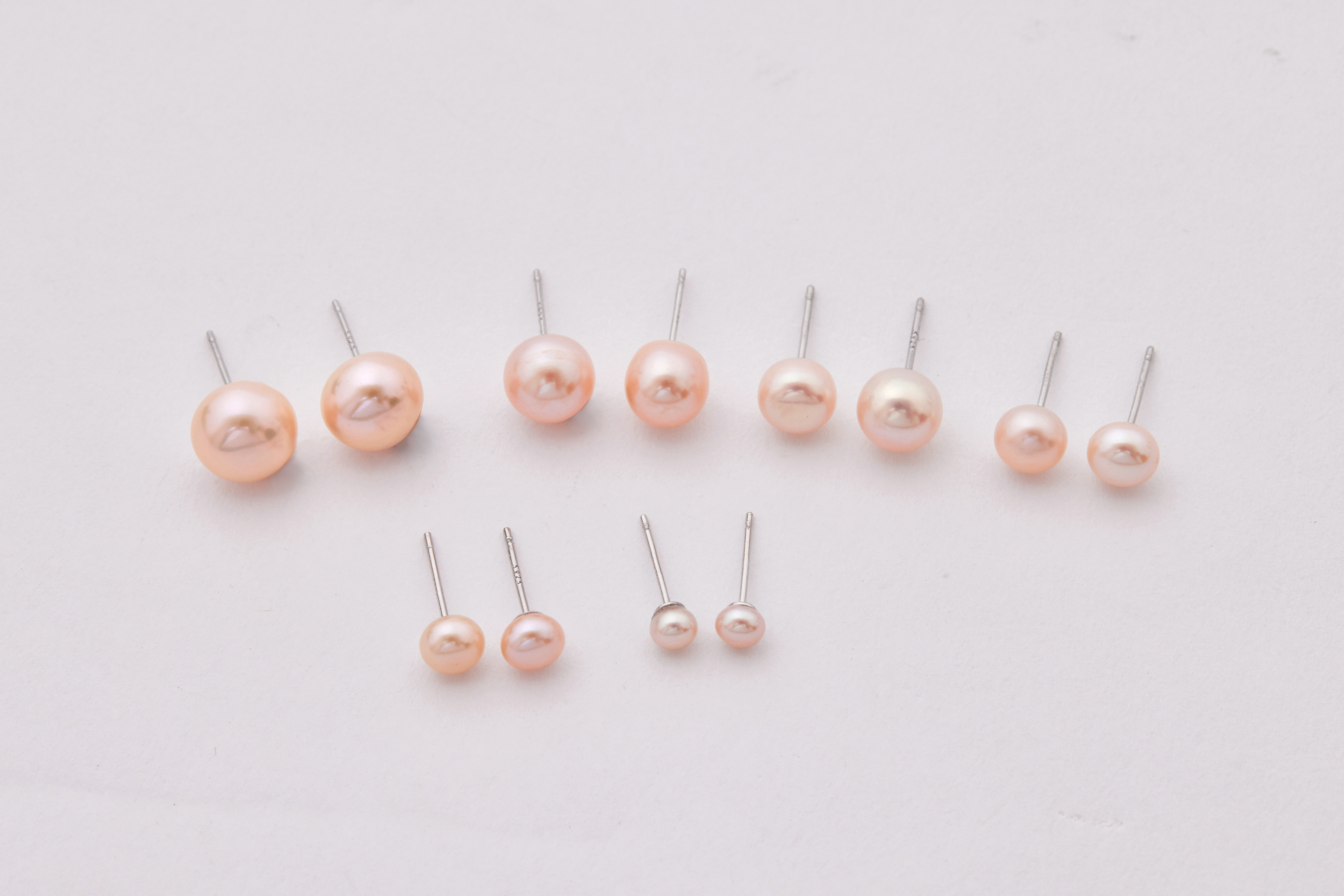 六種尺寸橘粉淡水珍珠耳環合照，依序展示 4mm 至 9.5mm 珍珠大小與光澤變化