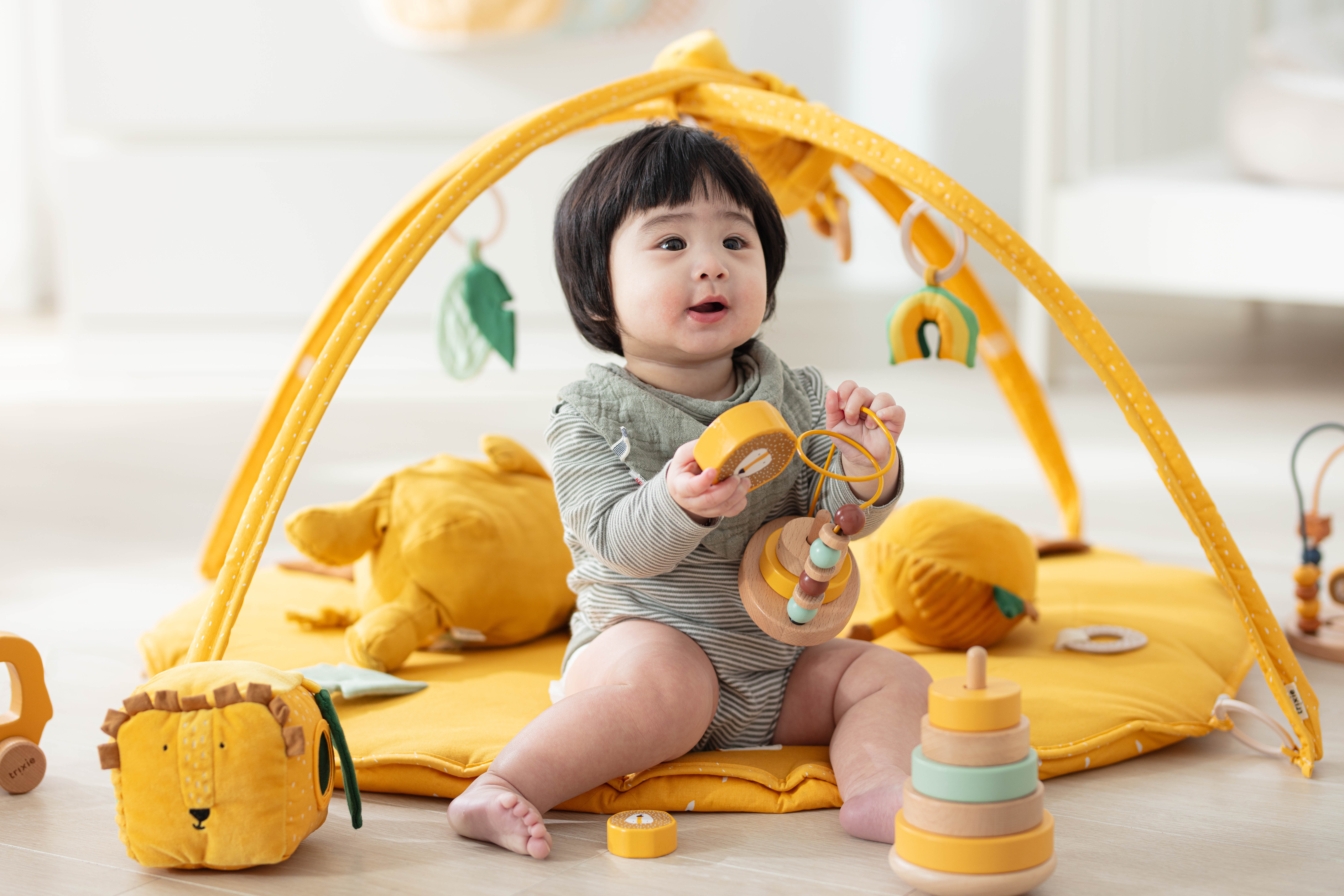 1歲寶寶坐在遊戲墊上操作感統玩具，訓練手部動作與專注力，背景為暖黃色感統遊戲區與木質玩具。