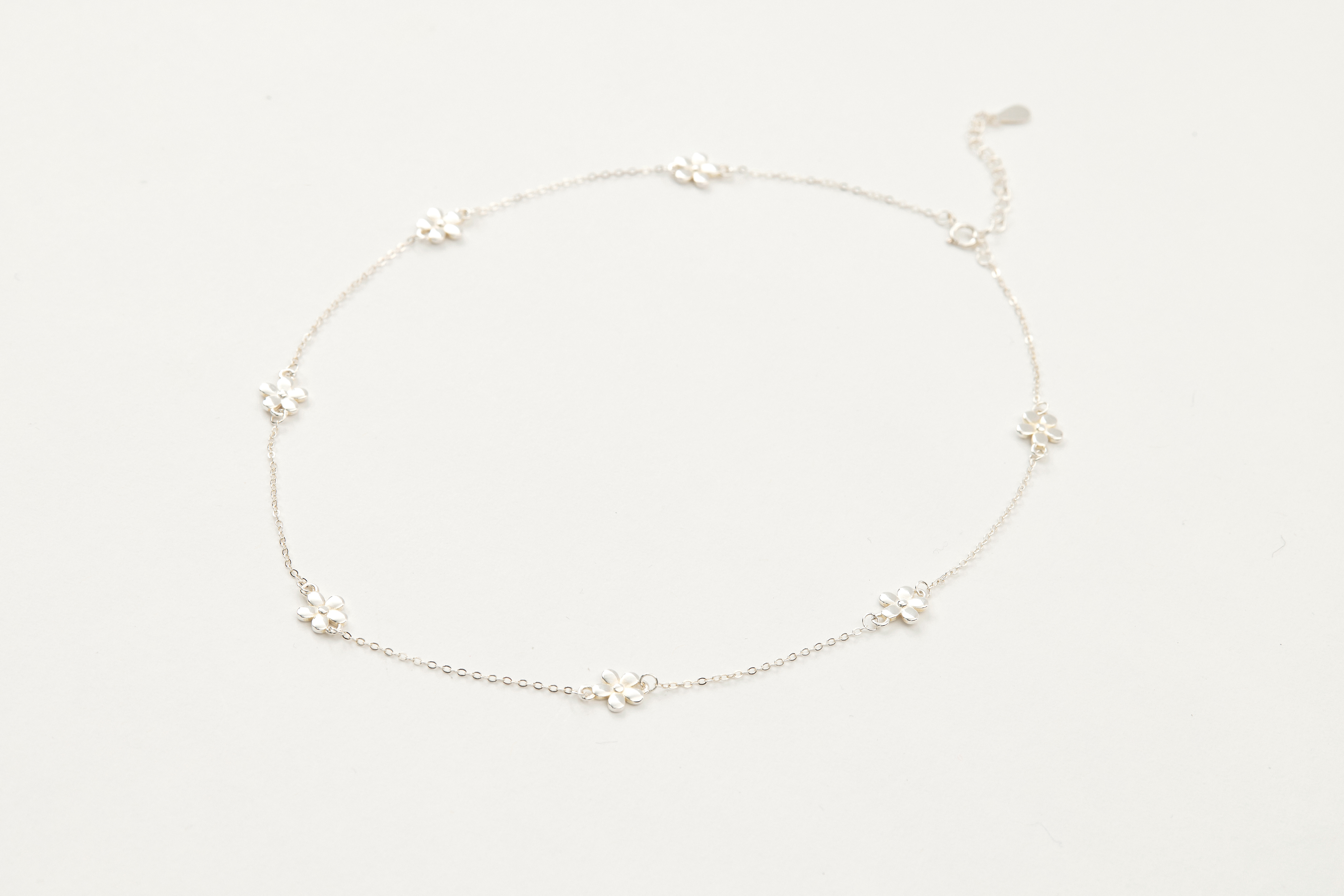 小花項鍊自然平放於桌上，純銀閃耀光澤細膩動人。