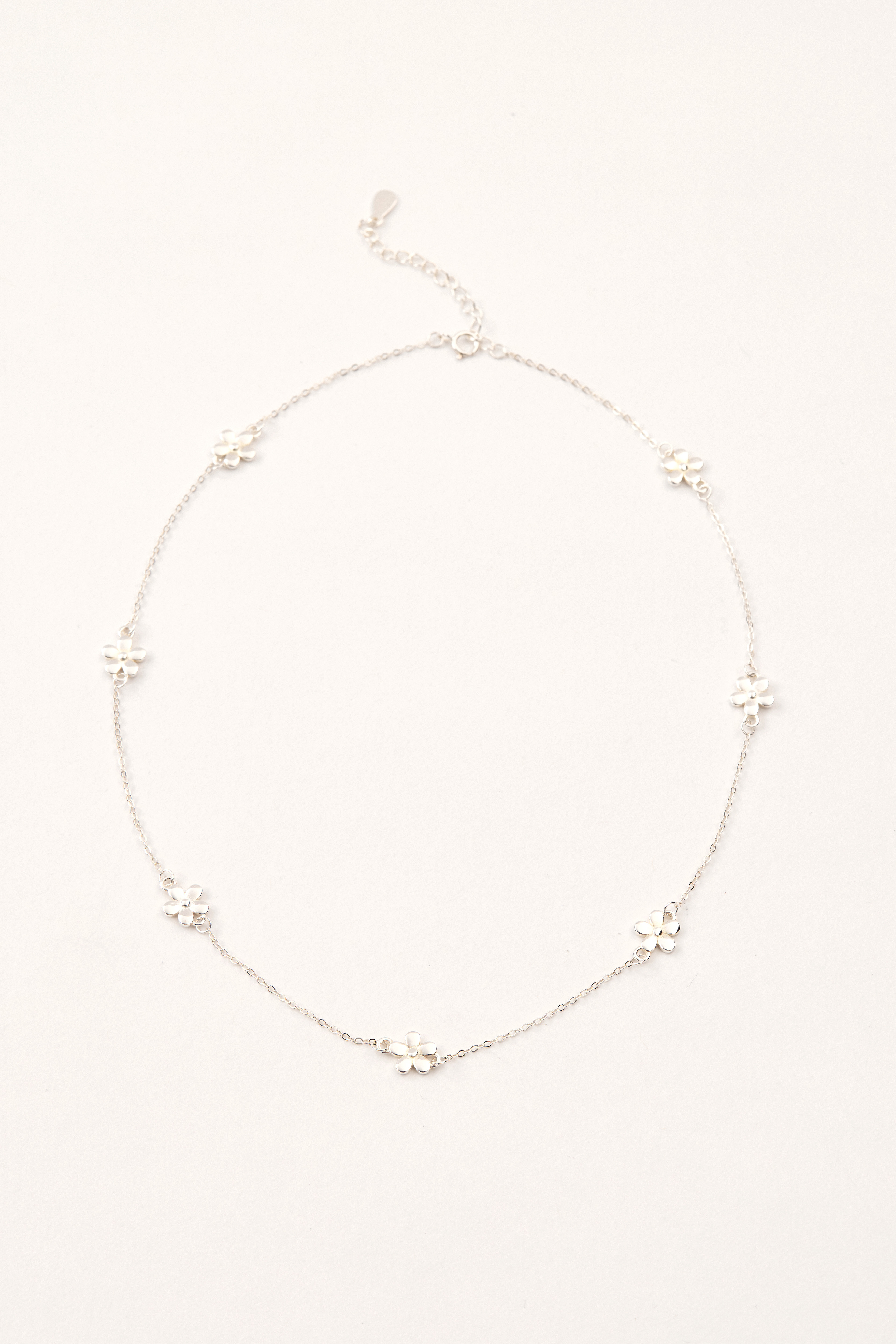純銀小花項鍊平放於白色布面上，展現小巧細緻的花朵墜飾與細緻鍊條。