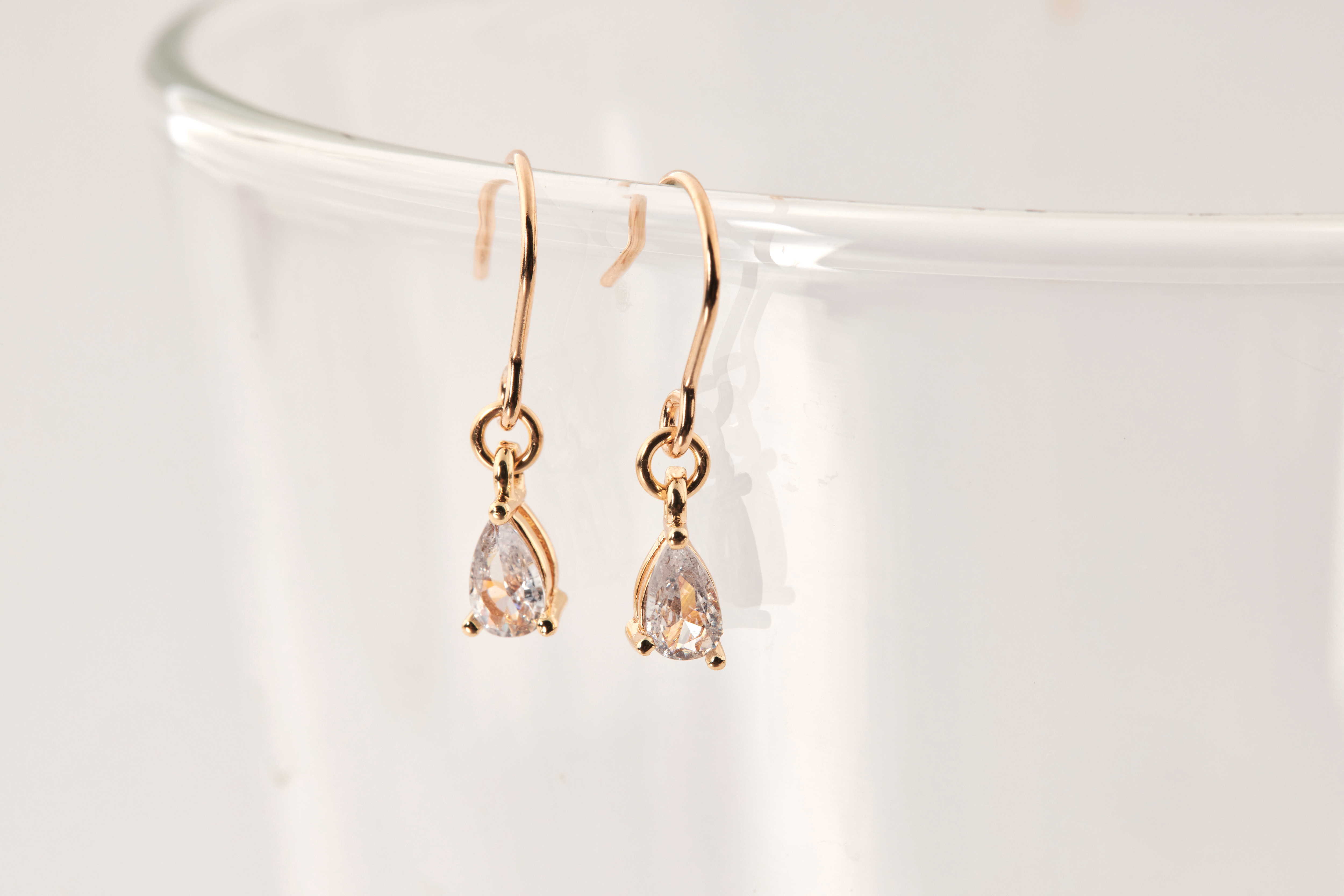 耳環垂掛於透明展示架上，水滴鋯石在光線下閃爍細膩光芒，展現高級質感。