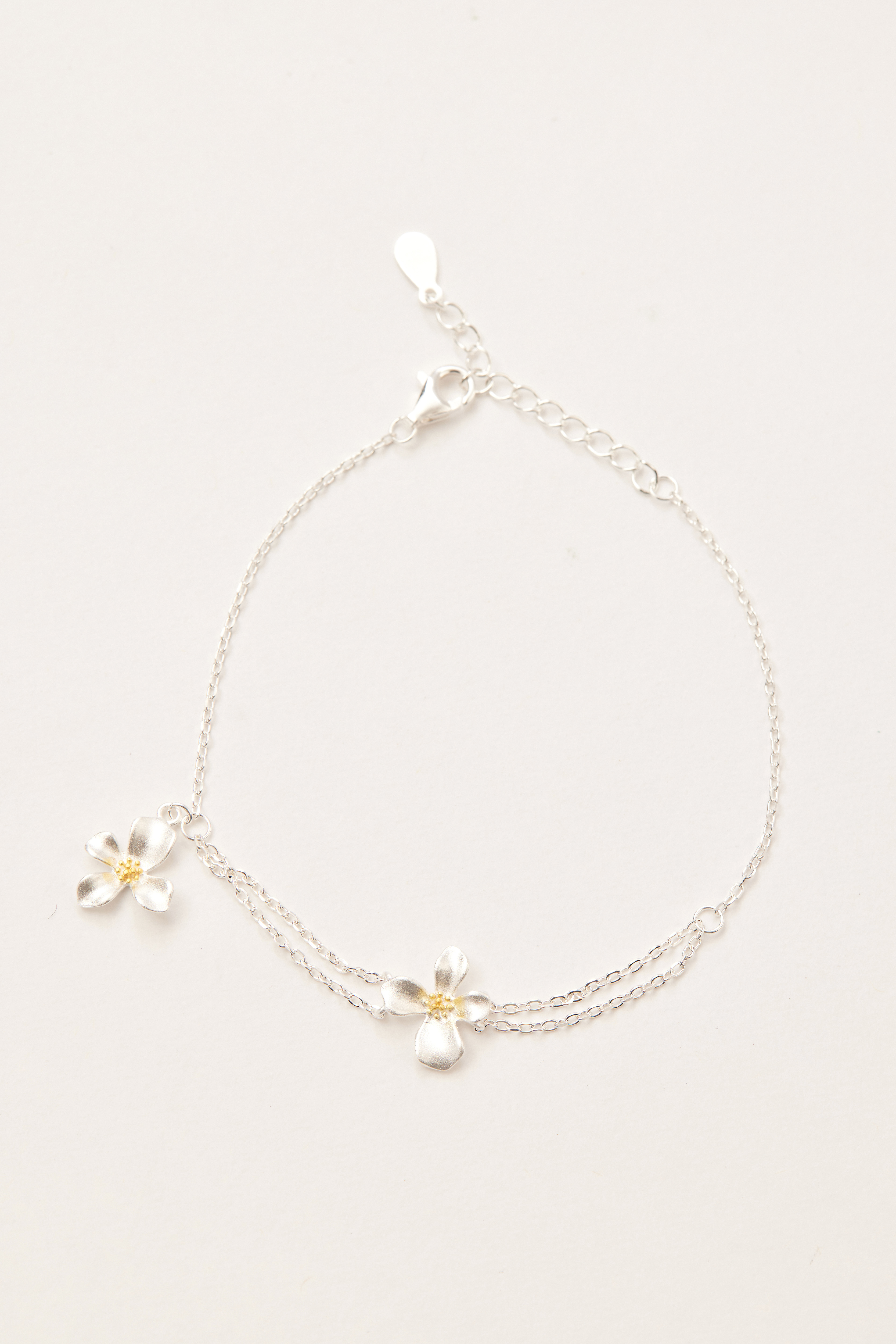 純銀雛菊小花手鍊平放於素面背景上，細緻花朵墜飾串連整條鍊身，設計清新可愛。