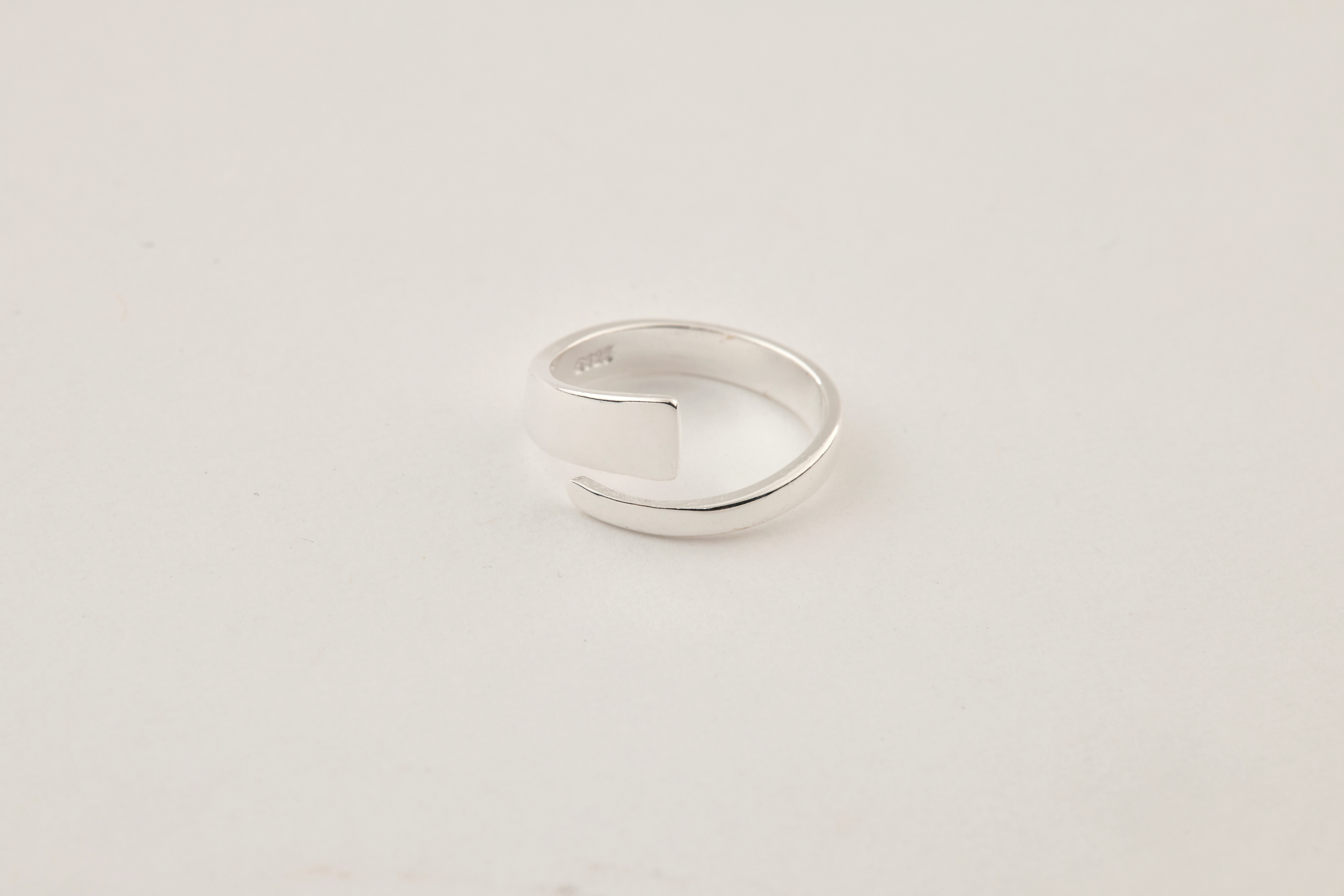 戒指平放於素面桌上，純銀質地光滑鏡面反光，開口設計小巧精緻。