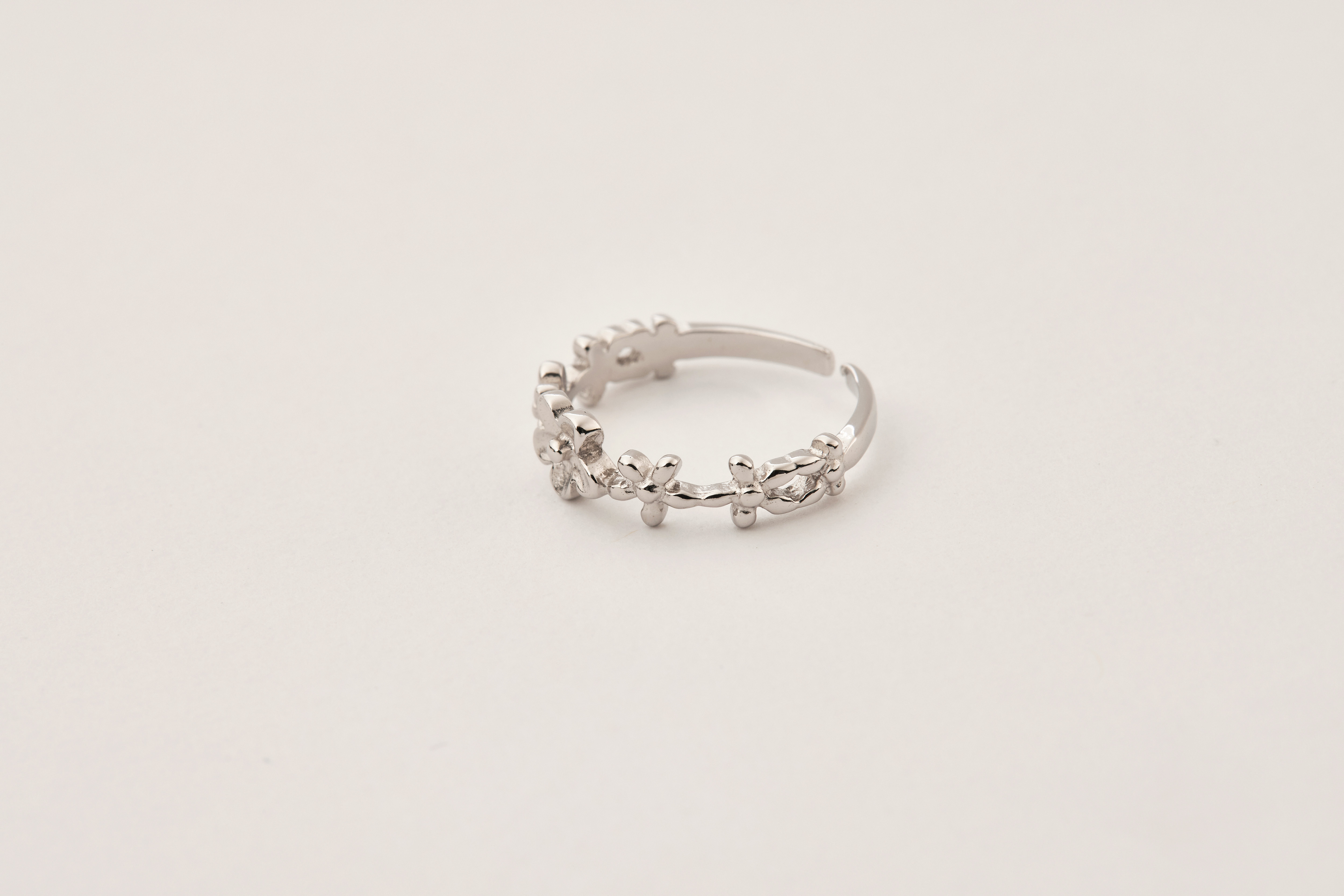 尾戒平放於素面桌上，花朵造型精緻可愛，純銀材質反射柔和光線，質感溫潤。