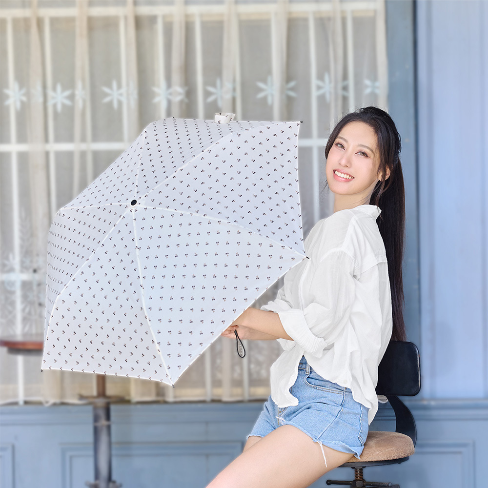 一位長髮女子坐在咖啡廳窗前,微笑著展示一把白底印花的輕便摺疊傘,穿著白襯衫與牛仔短褲,展現輕鬆清新的日系風格。