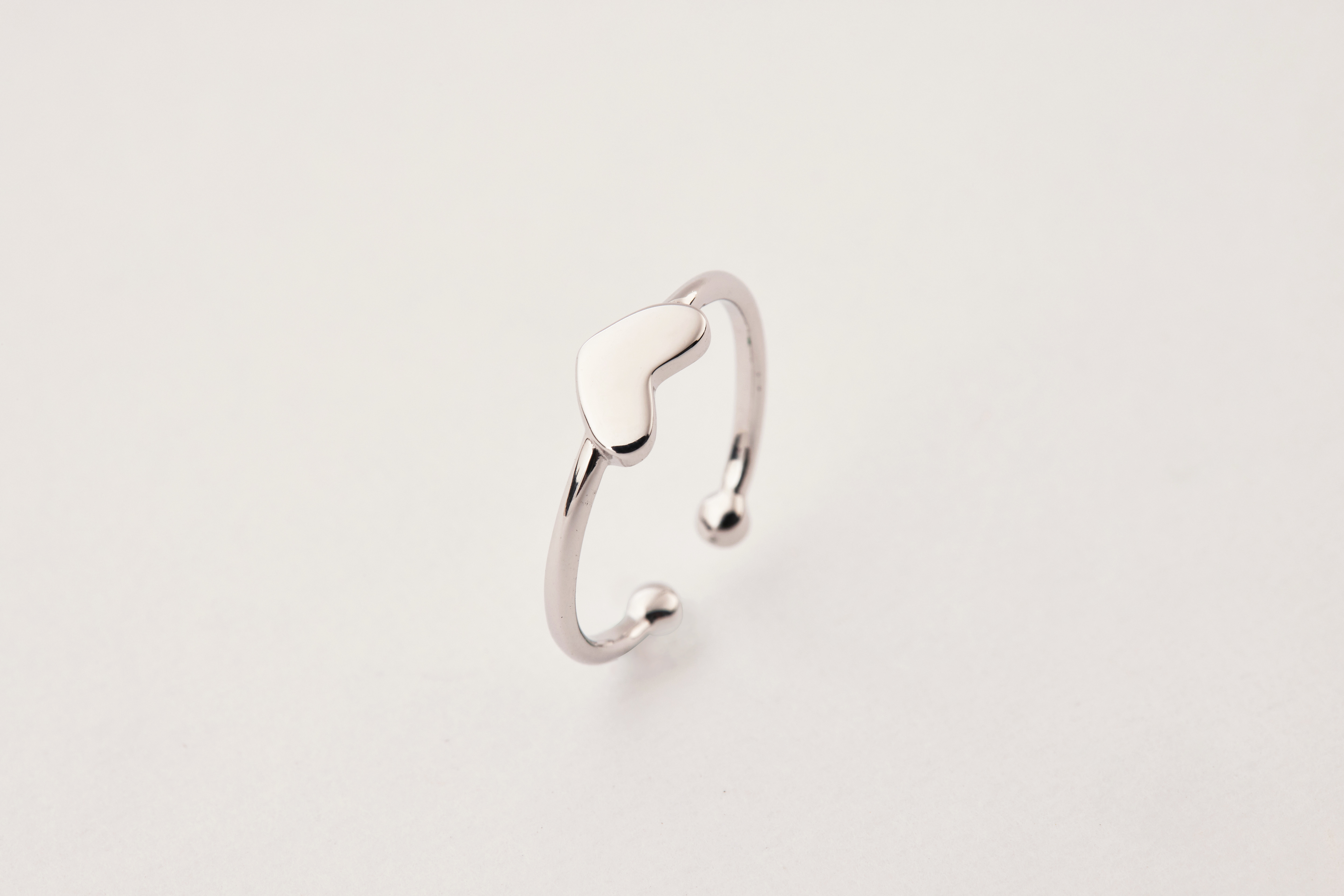 純銀愛心尾戒立於白色桌面上，愛心造型鏡面，反射出細膩光澤。