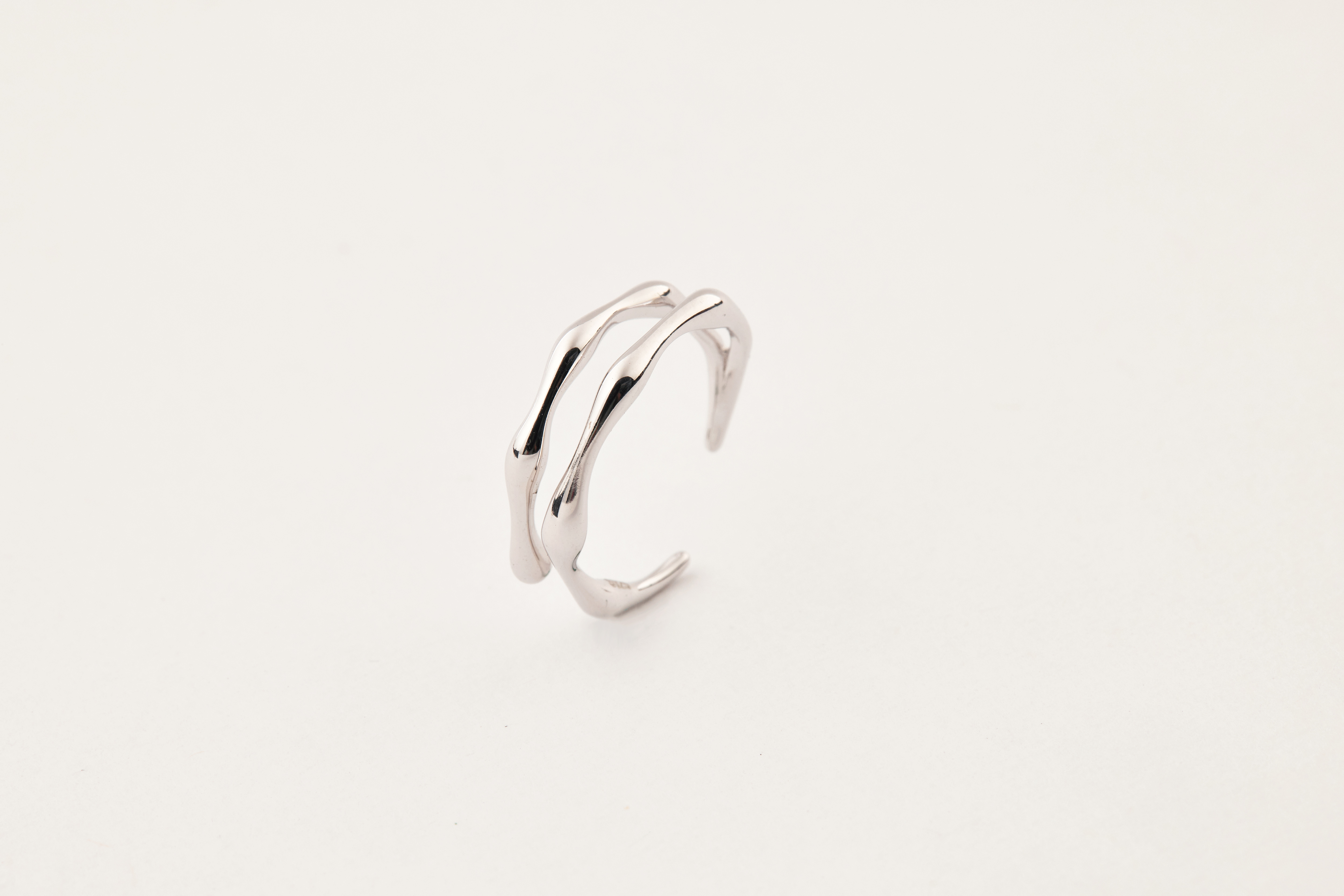 純銀流線尾戒直立擺放，戒身線條蜿蜒流暢，展現極簡設計與金屬光澤。