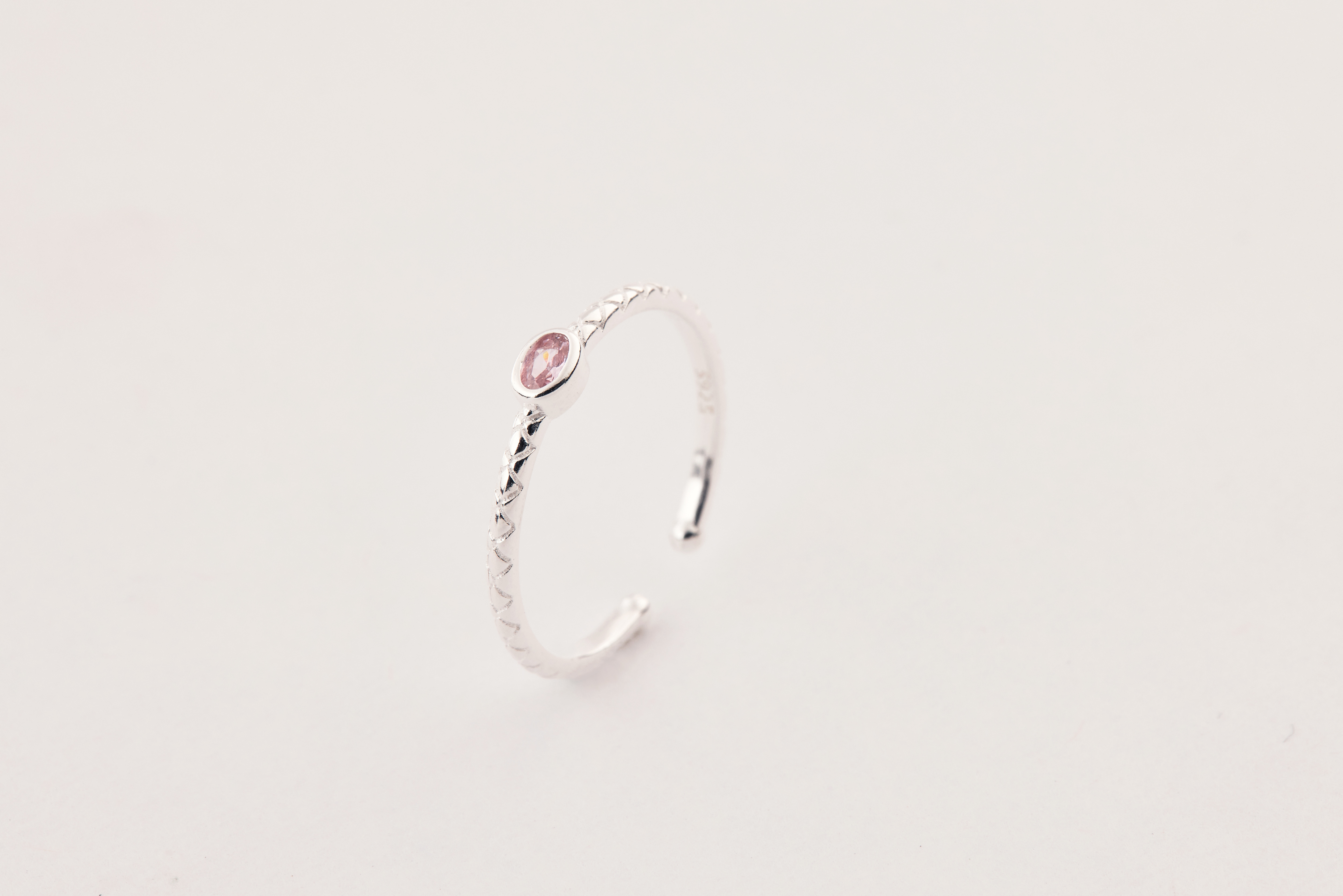 粉色鋯石戒指立於桌面上，主石閃耀柔和光芒，純銀戒身簡約包覆。