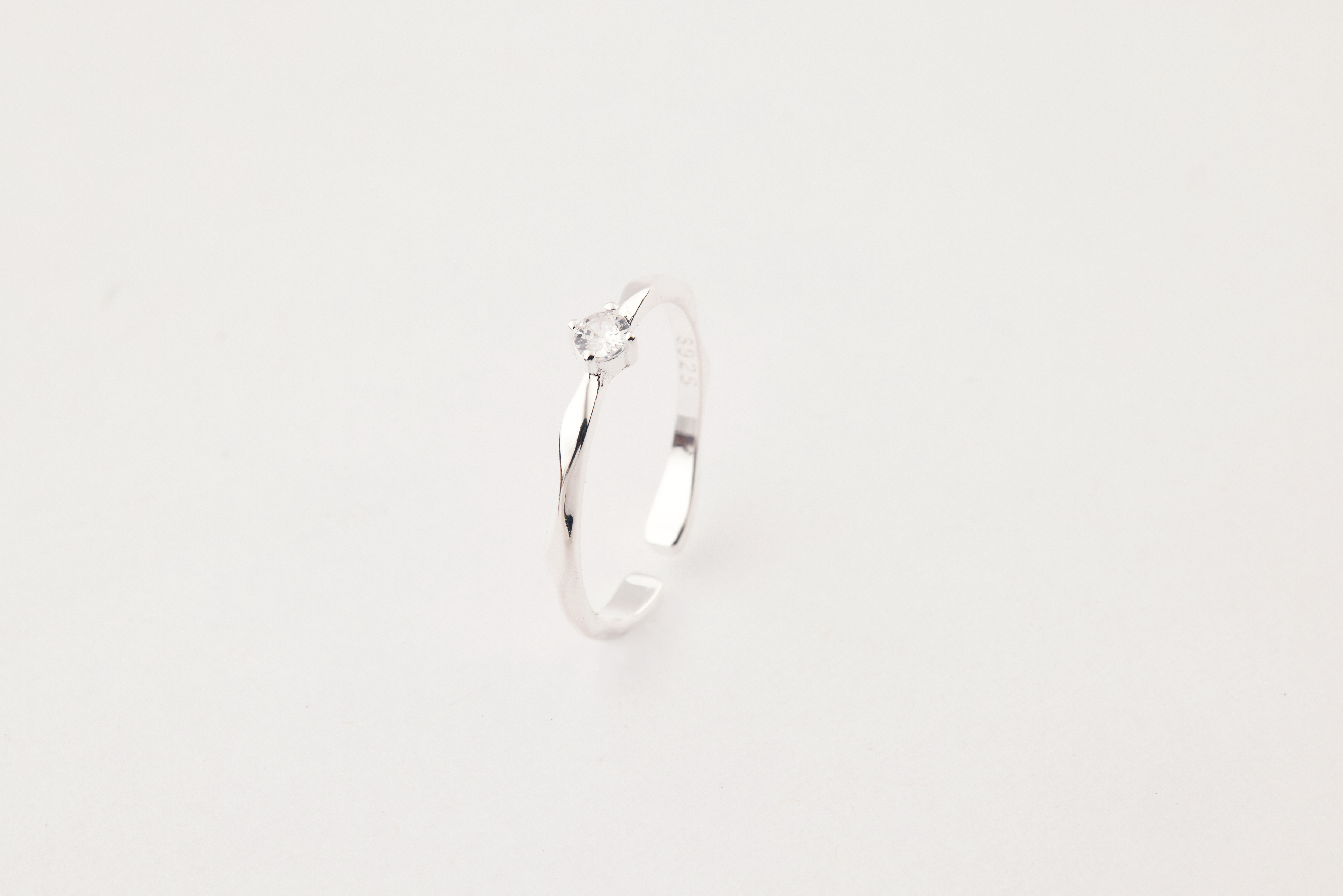純銀鋯石戒指立於白色背景上，中央圓形鋯石閃耀光芒，戒身線條簡約俐落。