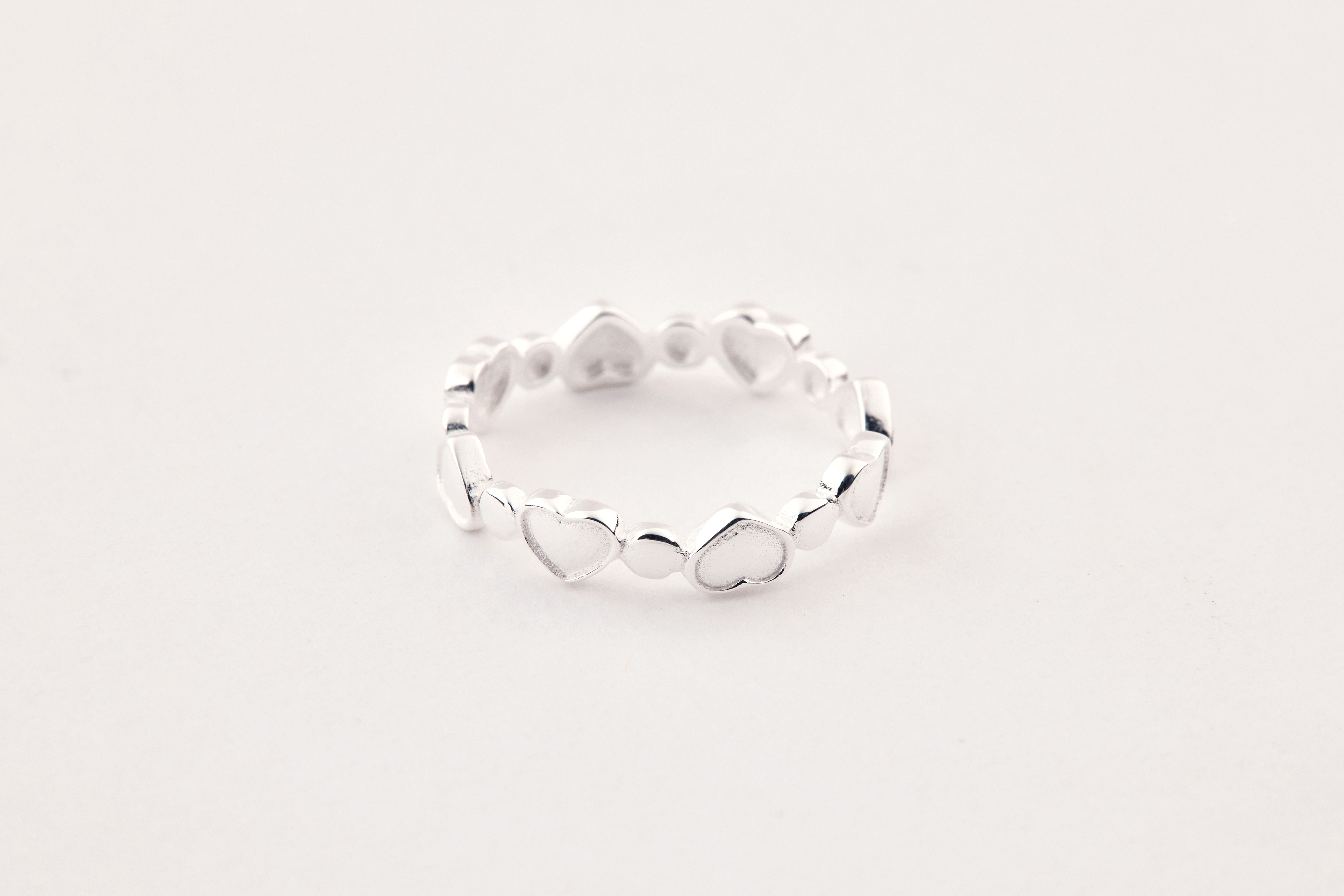 戒指平放於白色布面上，愛心造型細緻可見，整體風格清新柔美。