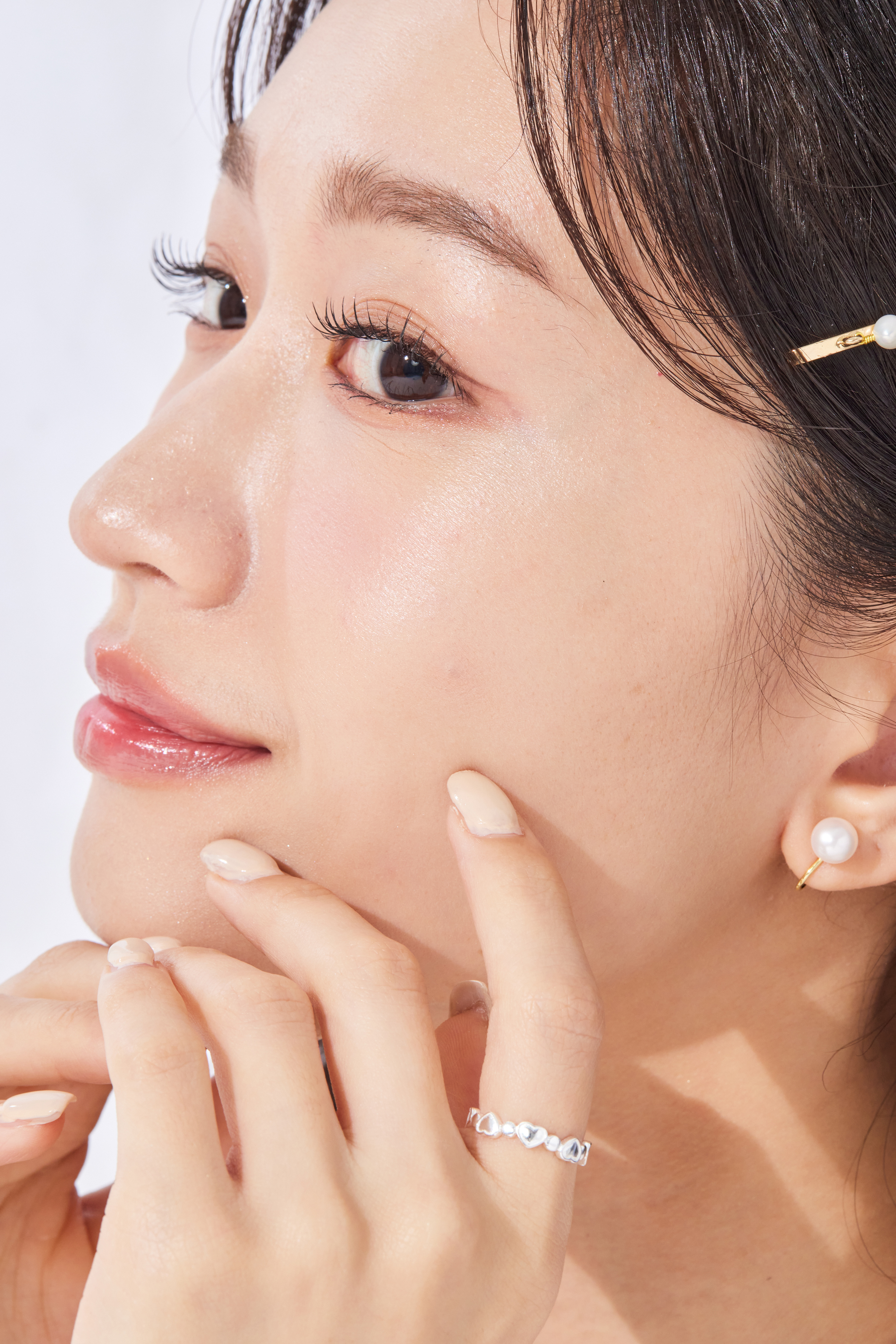 模特微笑輕摸下巴，純銀愛心戒指環繞於指節上，愛心造型隨光線閃爍，細節精緻吸睛。