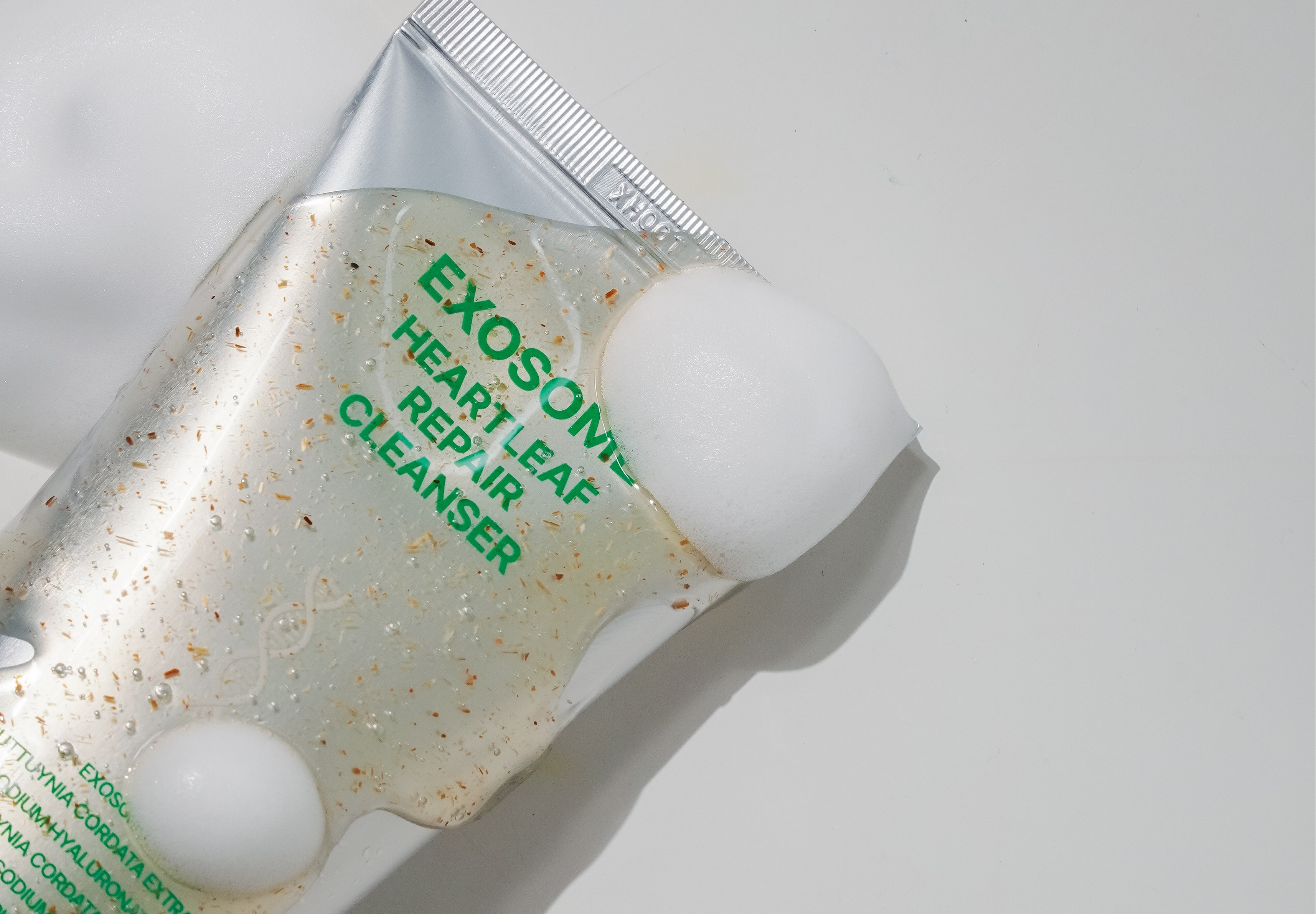 泌昇外泌體修護潔面乳擠出後呈透明凝膠狀，內含植萃顆粒與綿密泡沫，展現溫和清潔與去角質效果。