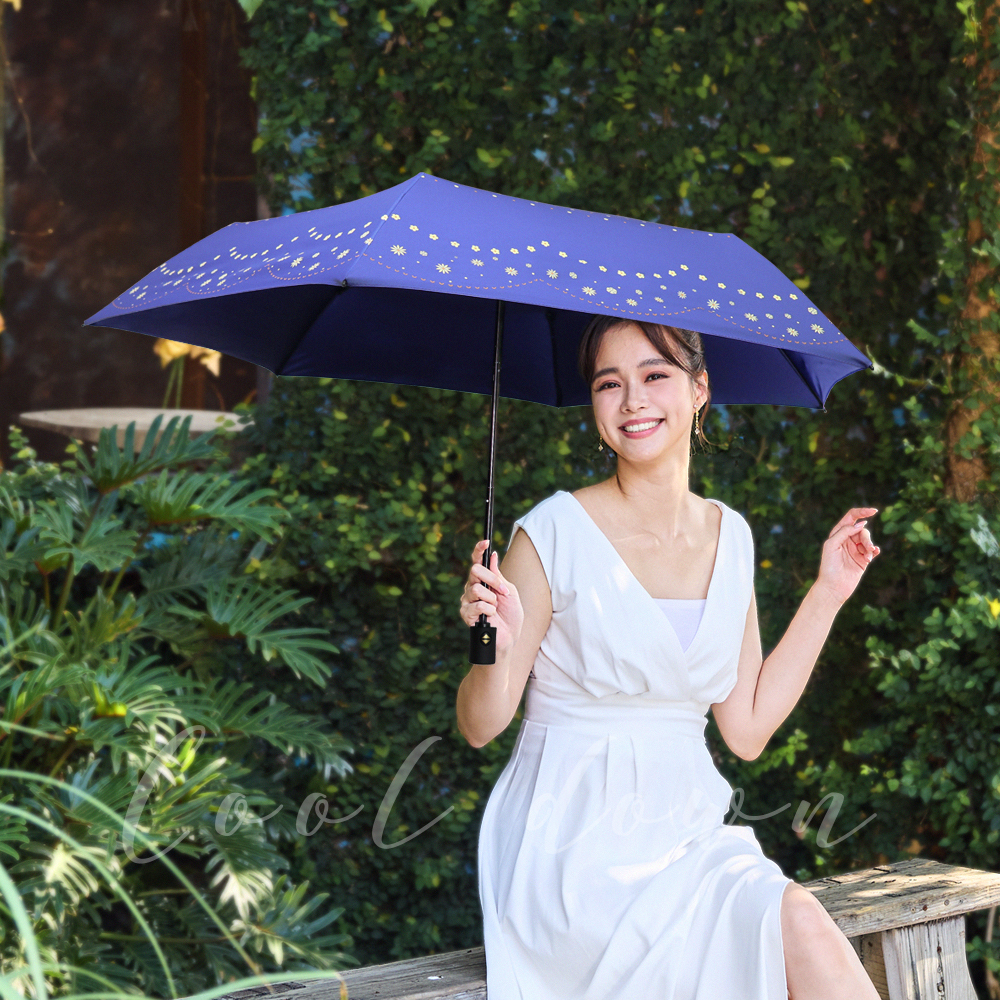 一位穿著白色連身裙的年輕女性開心地拿著環保紗降溫10℃自動傘水玉_藍紫坐在公園的長凳上