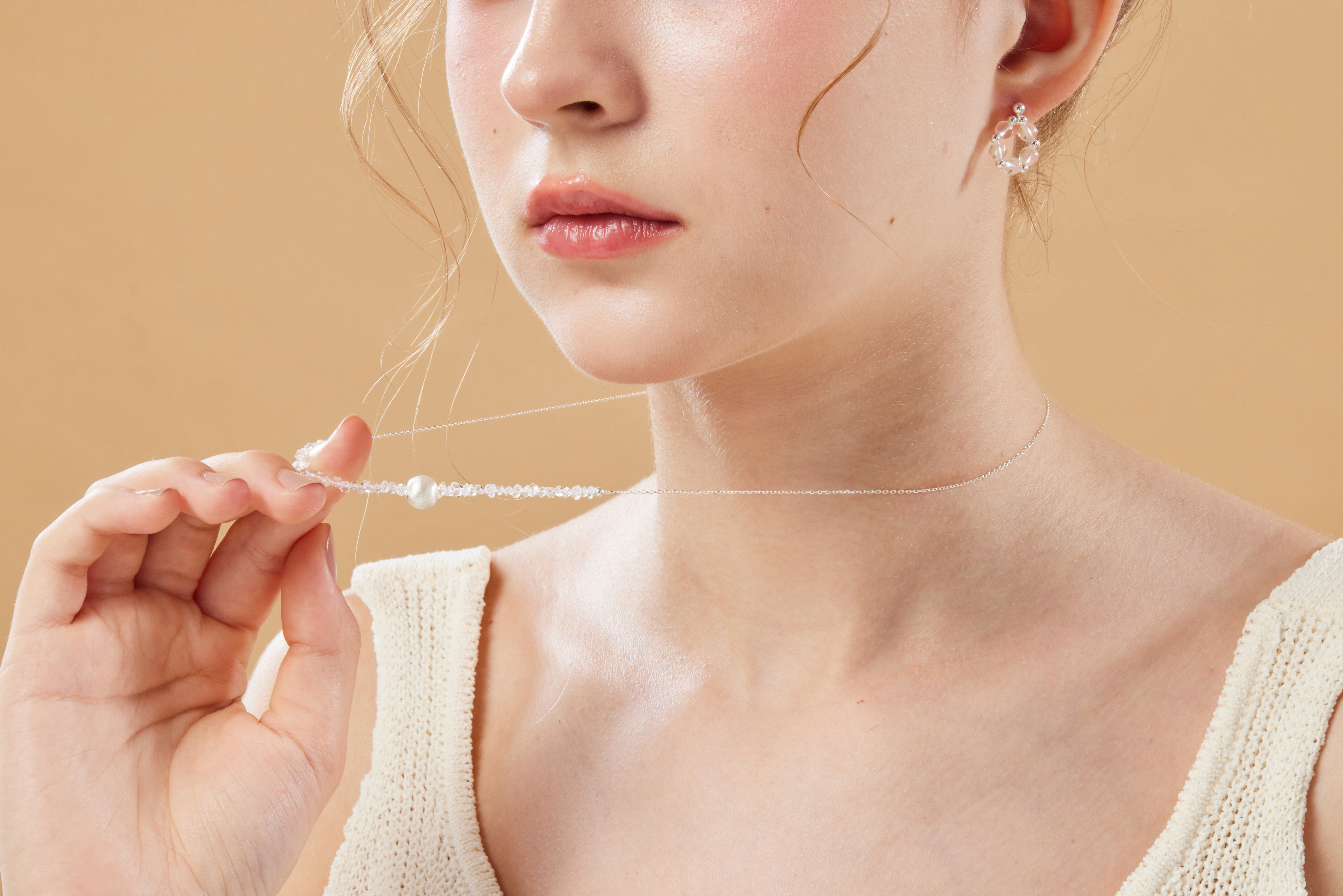 模特手扶項鍊特寫，鏡面銀球與半透明貓眼石閃爍自然光芒。