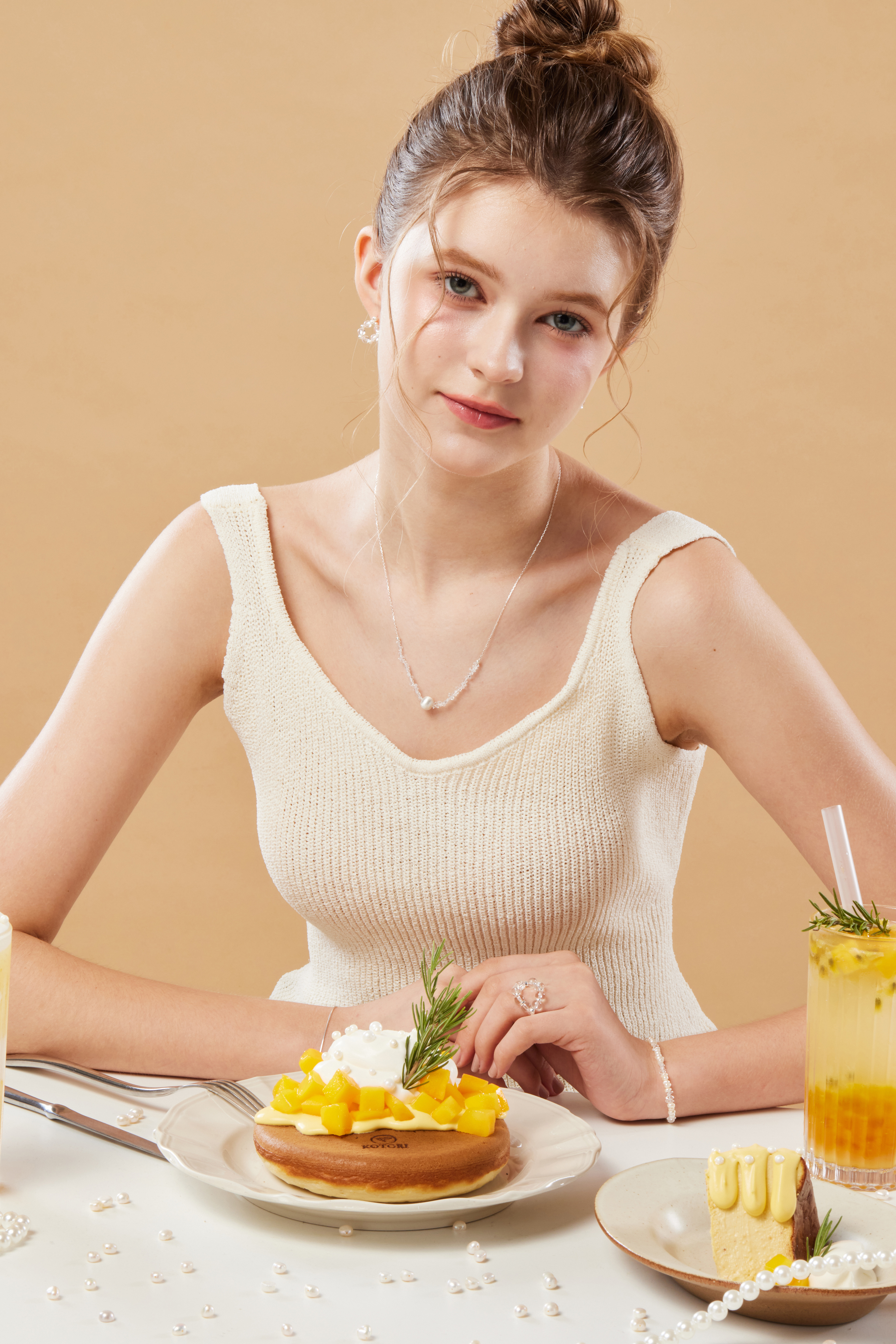 模特靠近桌邊，貓眼石項鍊在自然光與甜品背景中形成視覺焦點。