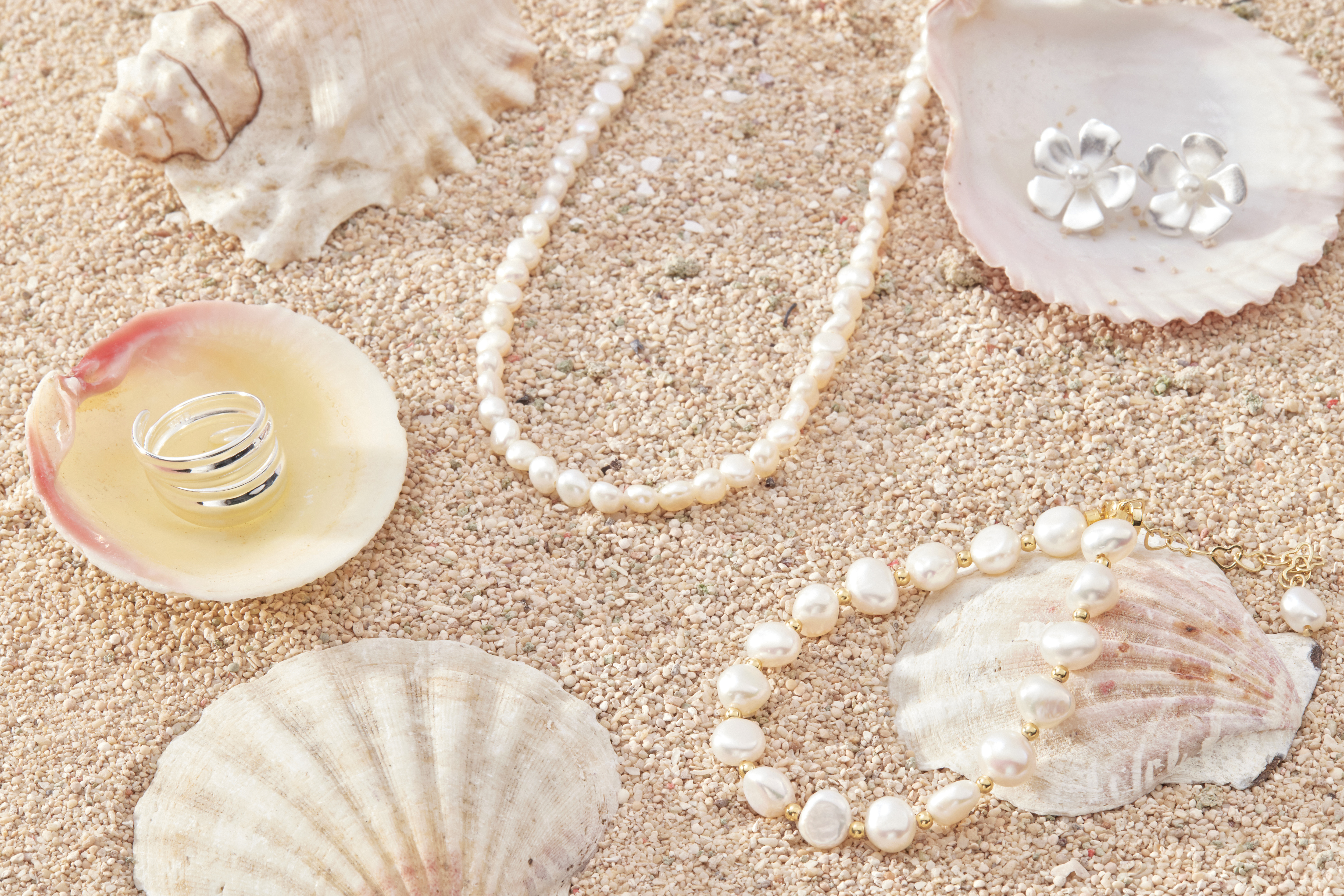 手鍊與純銀珍珠飾品一同擺放於沙粒與貝殼間，營造出海洋風格的夏日清新氛圍。
