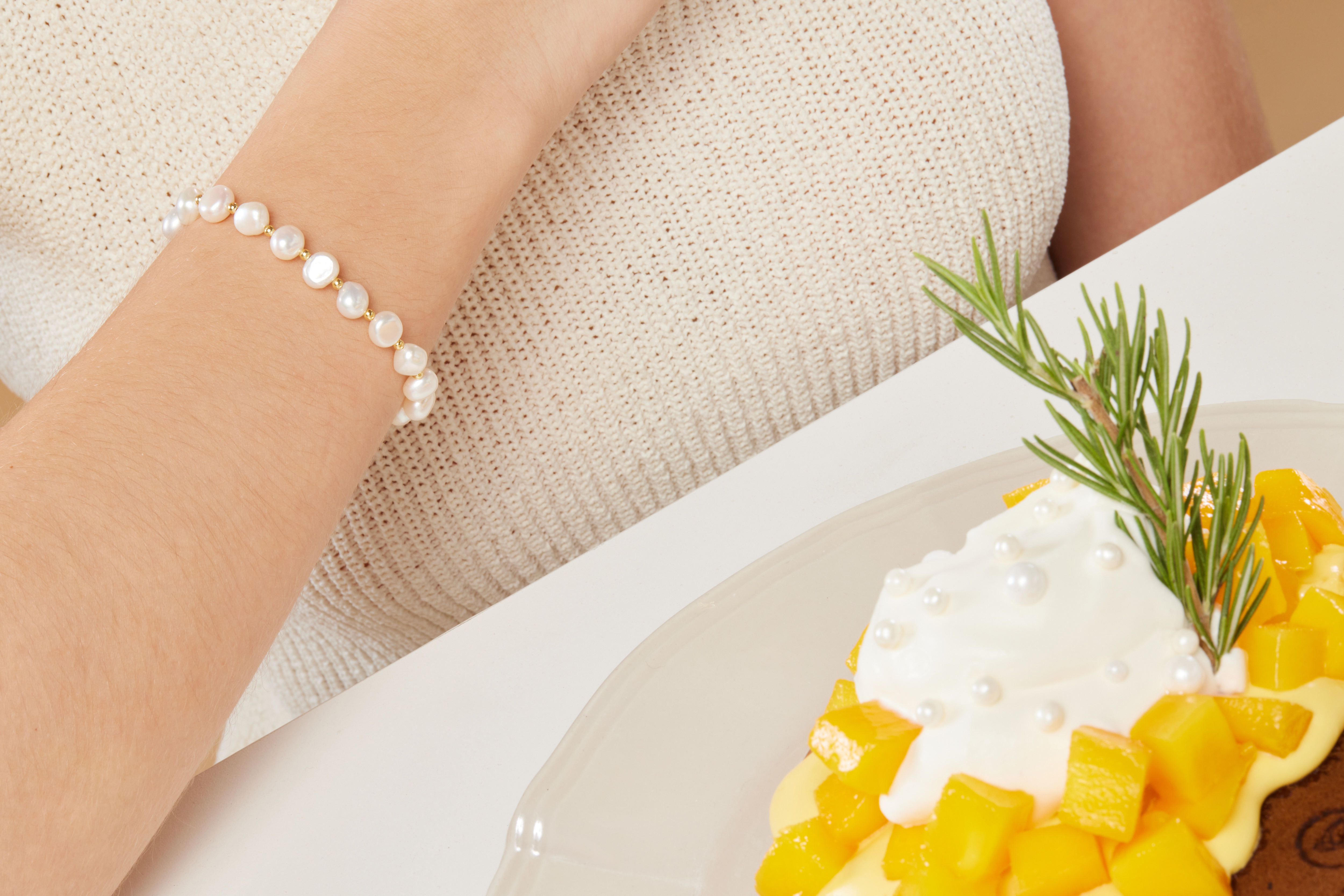 模特和甜點合照，珍珠手鍊成為手部亮點，與甜點色調相呼應，充滿生活美感。