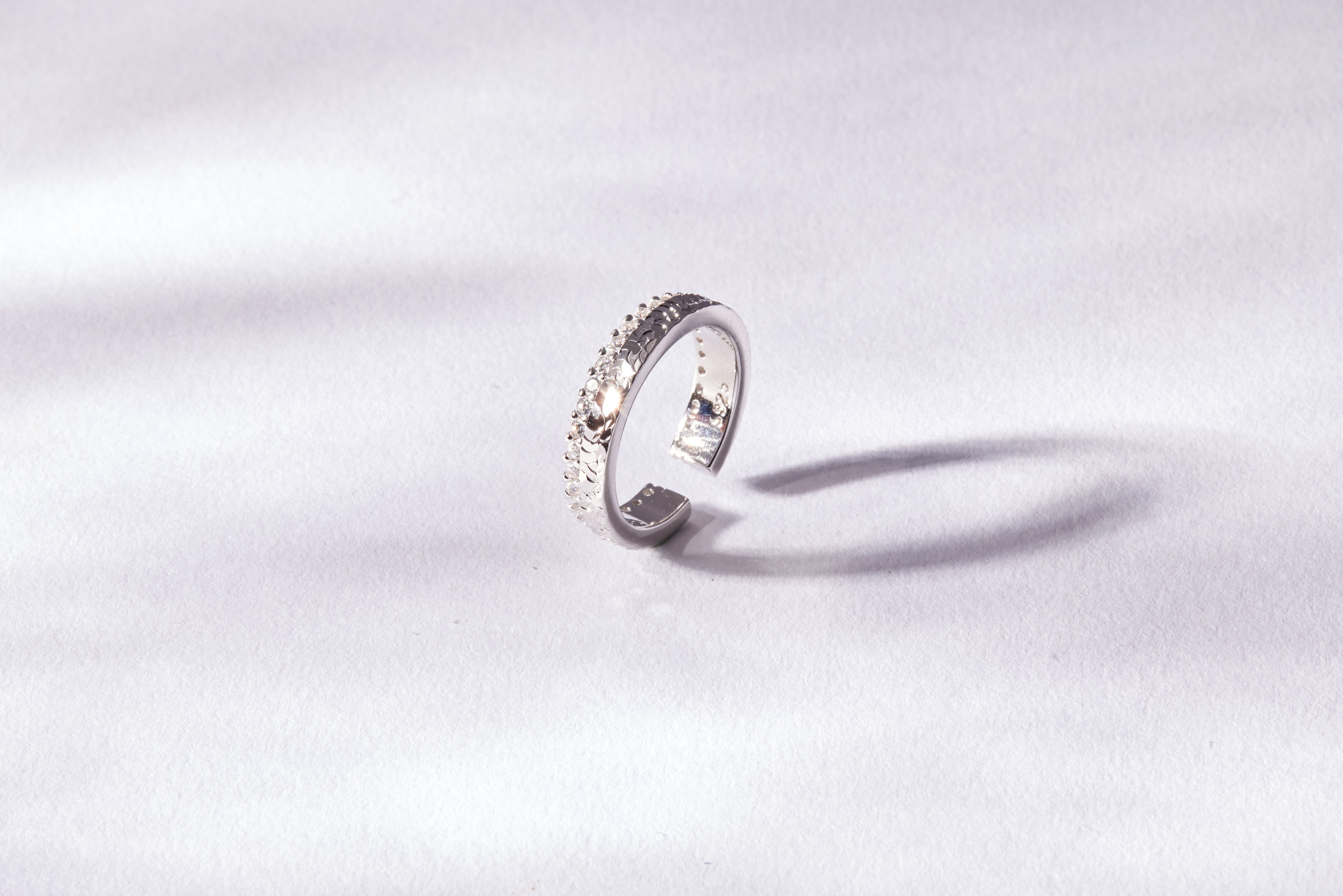 戒指立於白色桌上，鋯石呈現耀眼閃爍，整體設計經典優雅，適合日常佩戴。