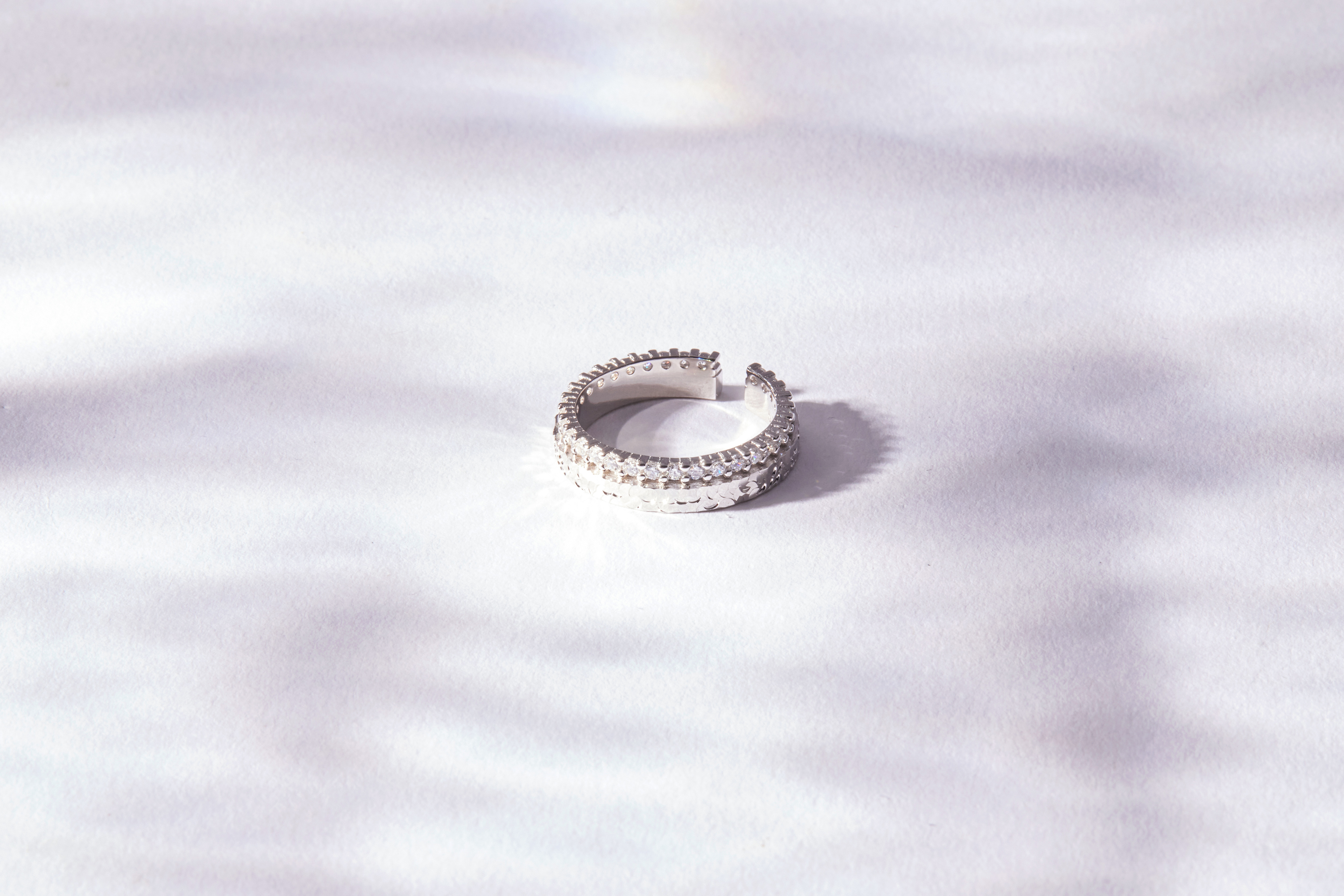 純銀閃亮鋯石戒指平放於柔霧布面，中央鋯石閃爍光芒，銀圈線條簡潔細緻。