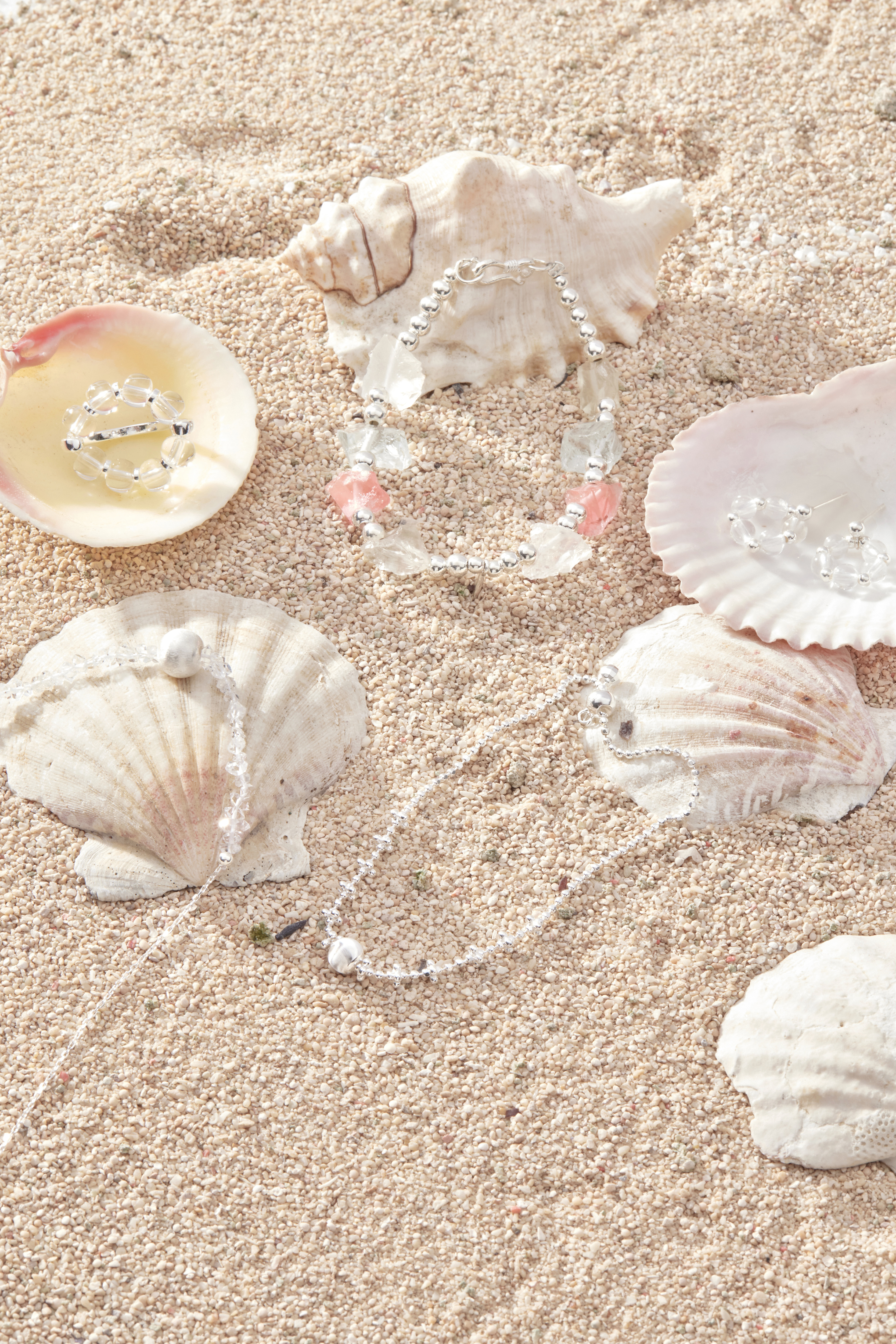 戒指與耳環、項鍊一同排列在海邊場景中，整體清透感呼應夏日主題。