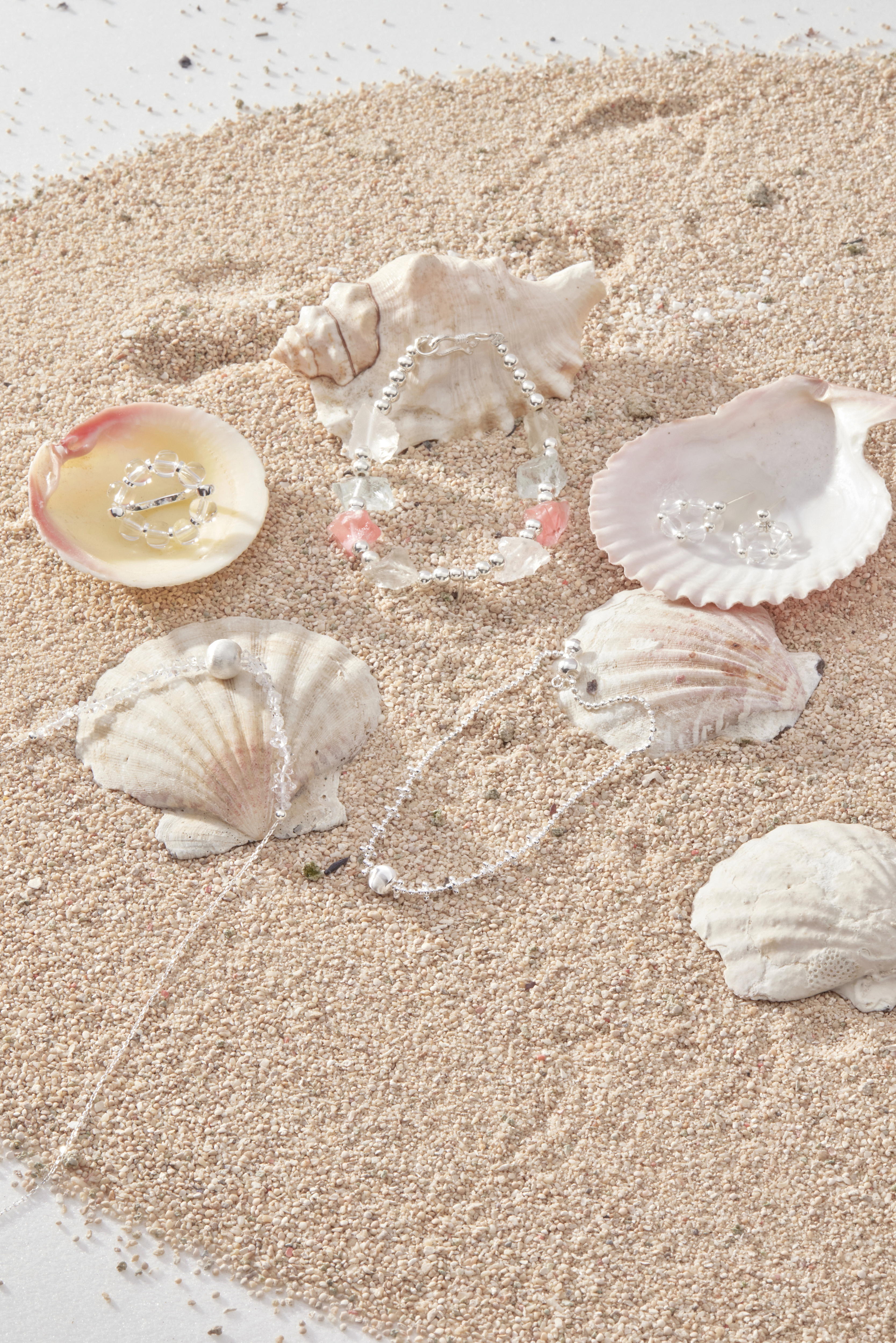 白水晶戒指與純銀飾品陳列在沙粒與貝殼間，呈現自然系海洋風格。