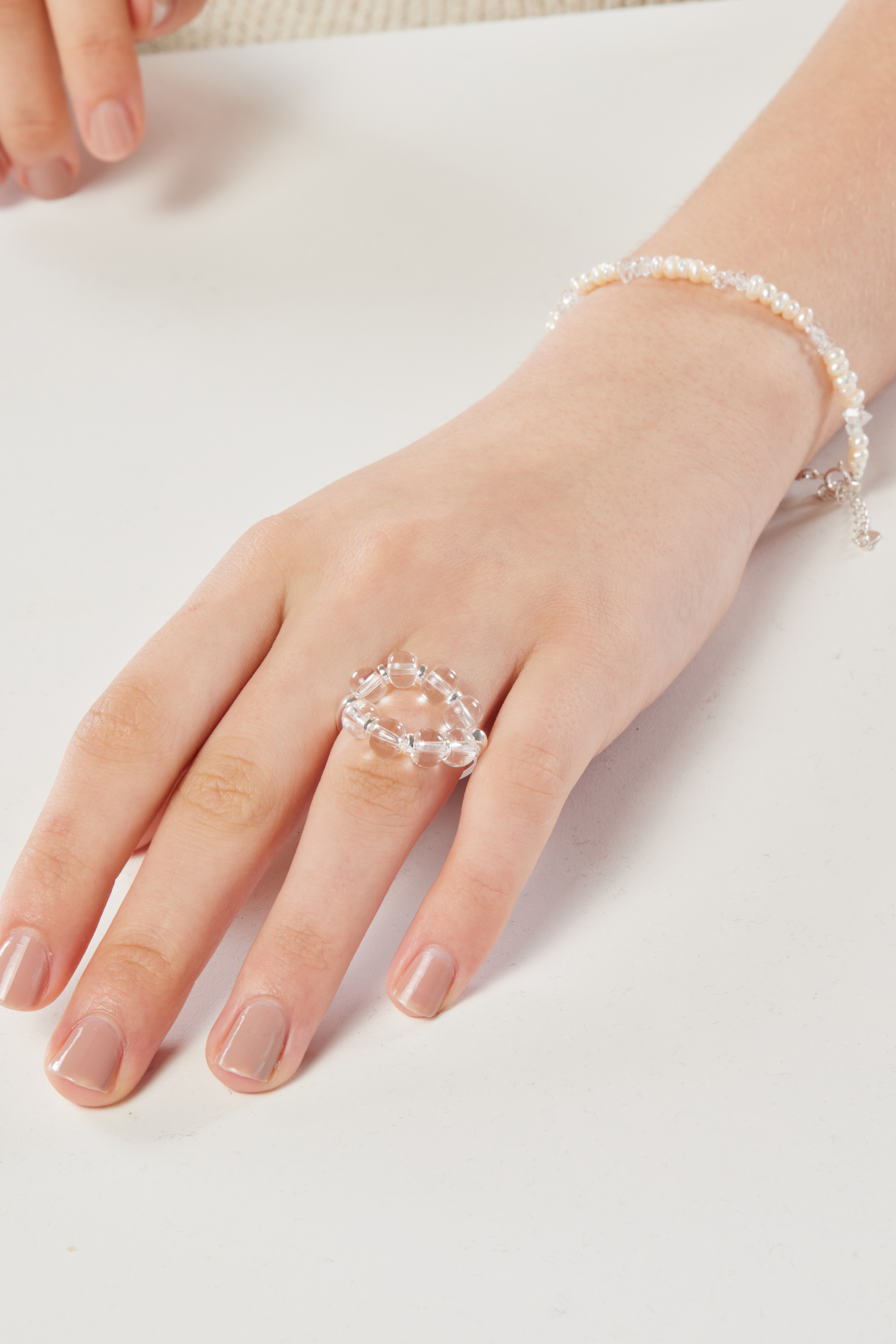 模特手放桌上特寫，白水晶戒指清雅映襯膚色，畫面簡潔柔和。