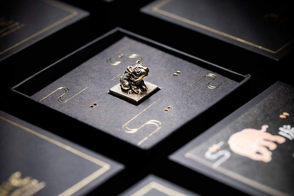 銅製十二生肖虎印章擺放於黑金工藝設計的展示盒中，背景為成套設計的包裝盒，展現細緻雕工與質感包裝的收藏氛圍。