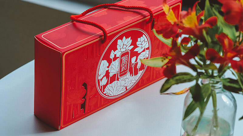 中秋節紅色禮盒搭配蓮花插畫設計與提繩，展現典雅與節慶氛圍，擺放於桌面搭配鮮花裝飾，送禮體面又喜氣