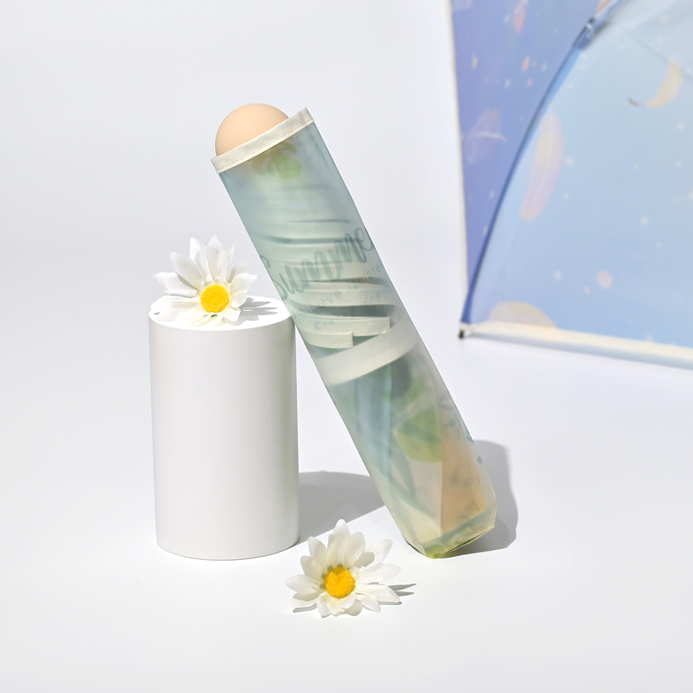 收合的夢幻透明摺疊傘-樹葉款斜靠在圓柱體的擺設旁邊,周圍還有小多的白色菊花點綴。