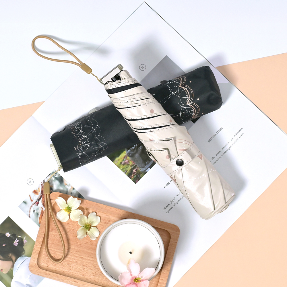 收合的兩把降溫10℃涼感扁摺疊傘_雪紡花放置於書上，旁邊放置日系的木質托盤及花朵作為點綴。