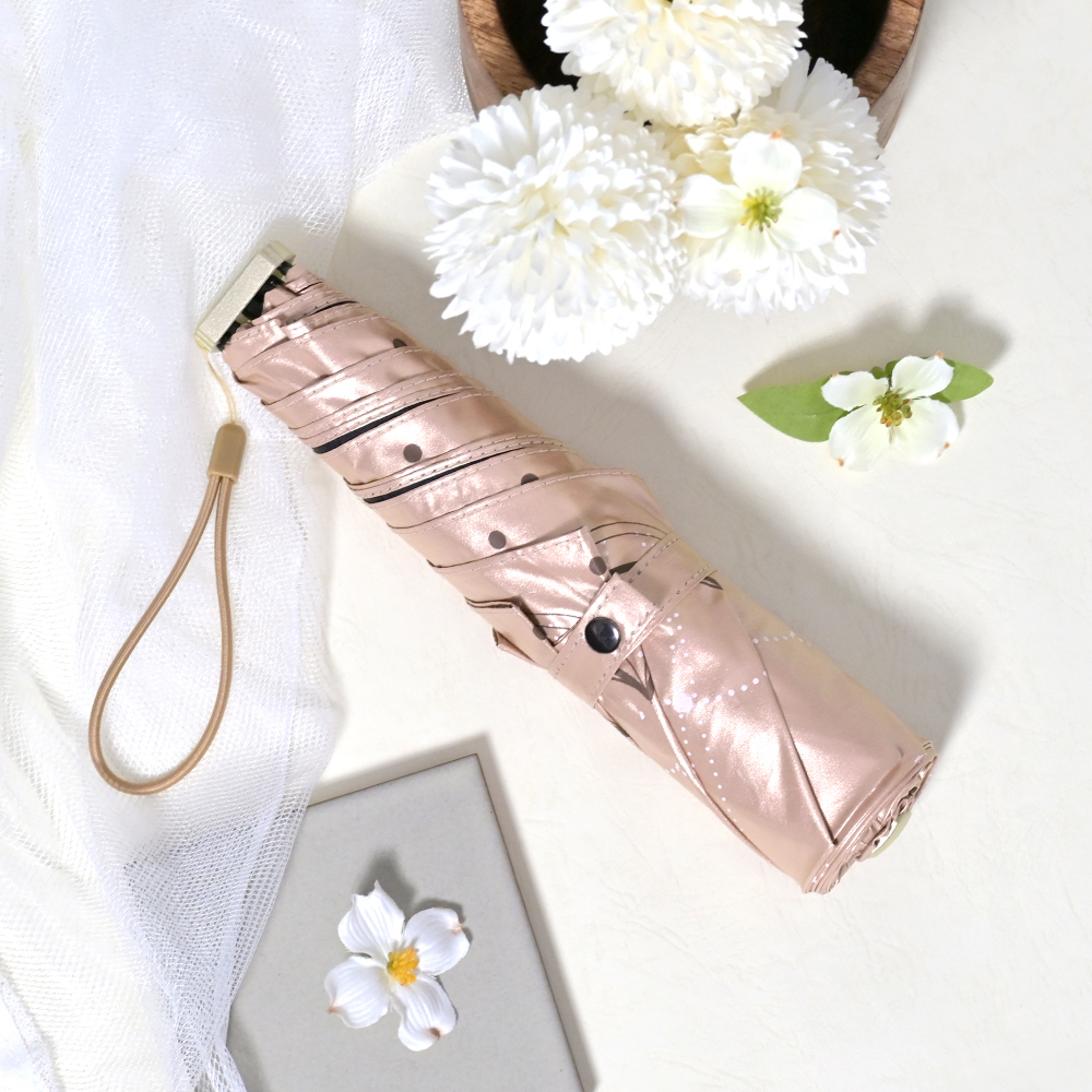 收合的降溫10℃涼感扁摺疊傘_雪紡花放置於白色的桌面，旁邊點綴著不同樣式的白色花朵。