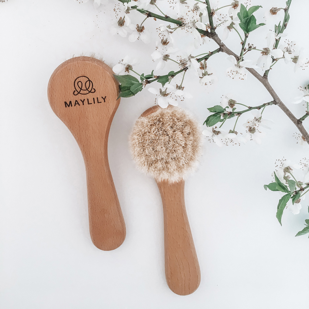 兩把 Maylily 嬰兒羊毛梳靜置於白色背景與花枝旁，圓潤木柄搭配柔軟刷毛，展現天然溫和的育兒質感。