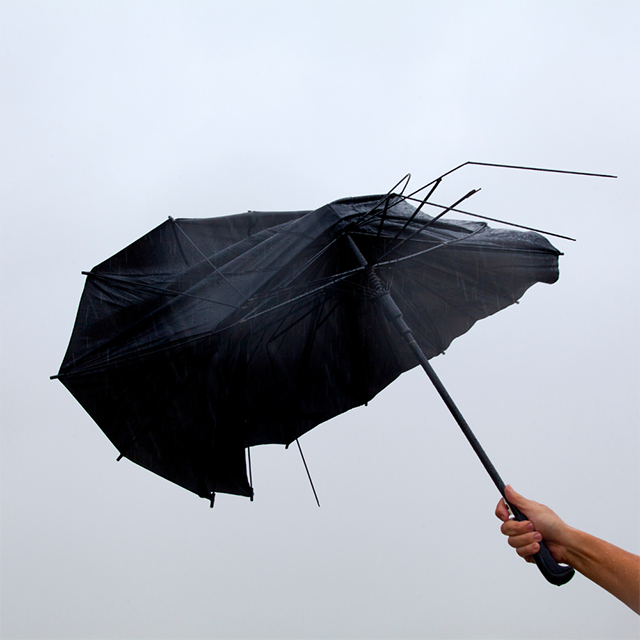 一隻手舉著被風吹斷傘架的黑色雨傘